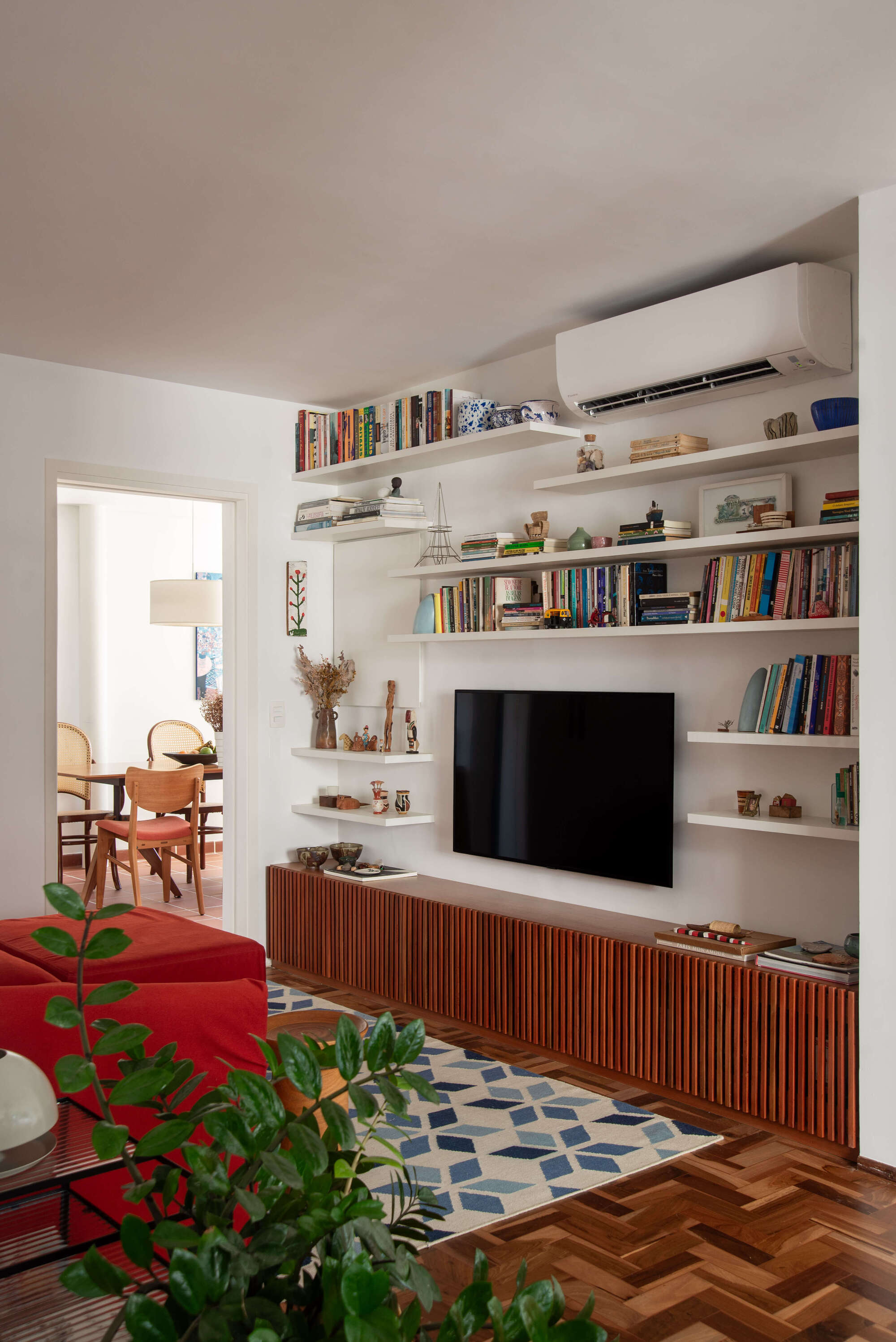 Built-in media wall with floating white shelves above a slatted wood cabinet beneath mounted television