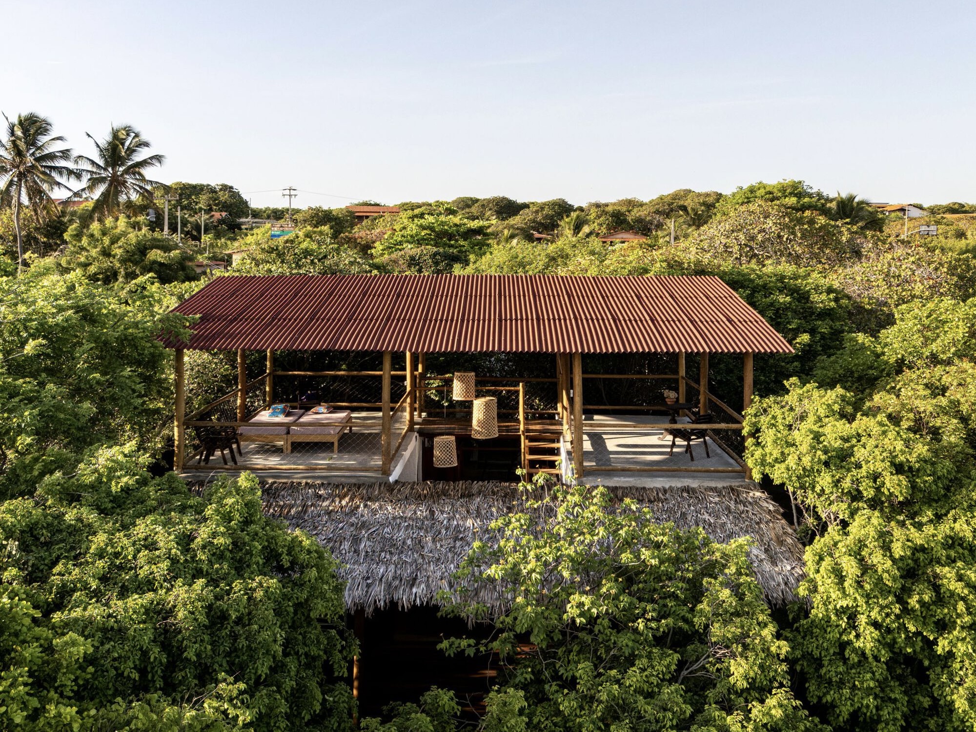 Aerial view of the timber-framed pavilion with corrugated metal roof nestled in dense coastal vegetation