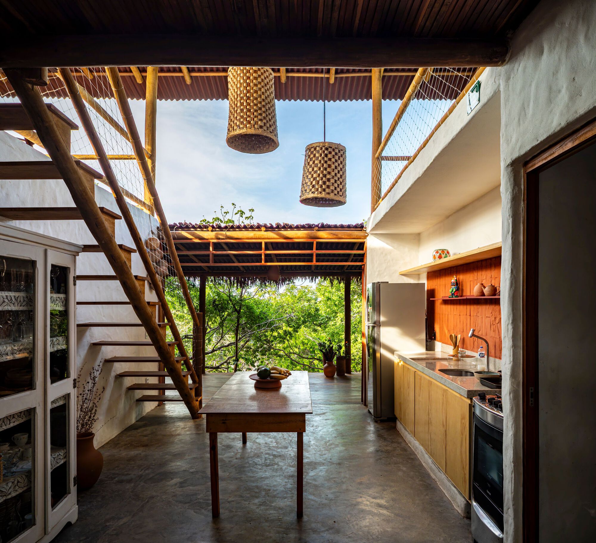 Interior kitchen with woven pendant lights and central table under a partial roof opening to sky