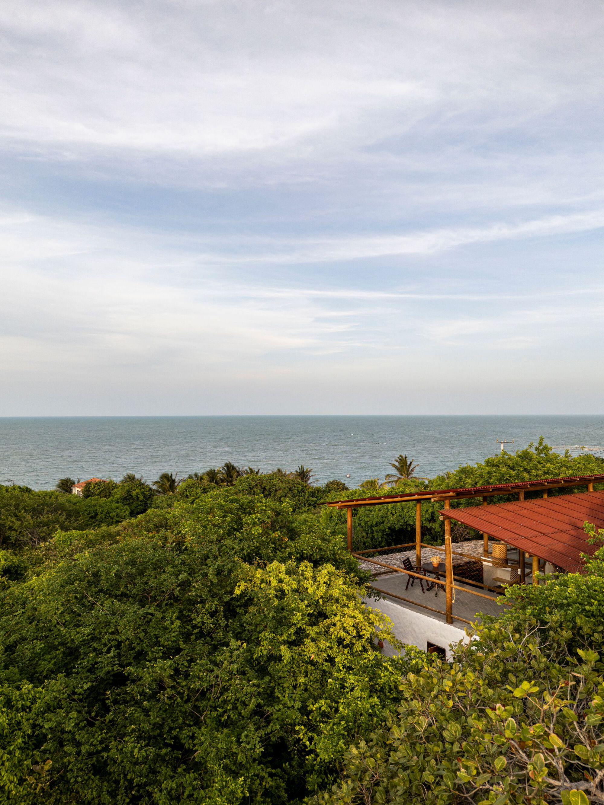 Elevated structure with timber pergola and red metal roof set among coastal vegetation overlooking the ocean