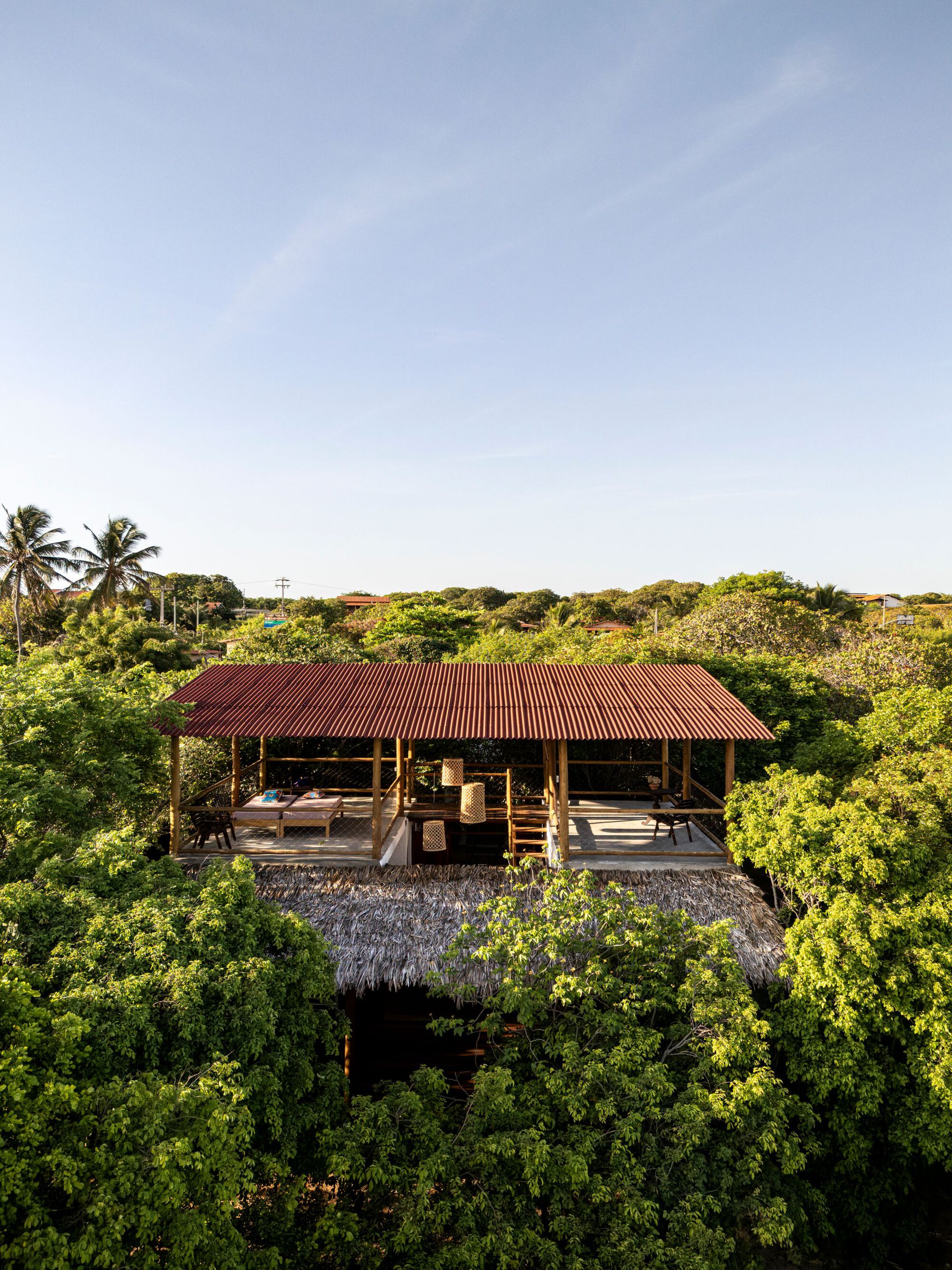 Frontal view showing the open-sided pavilion with red corrugated roof and timber columns among trees
