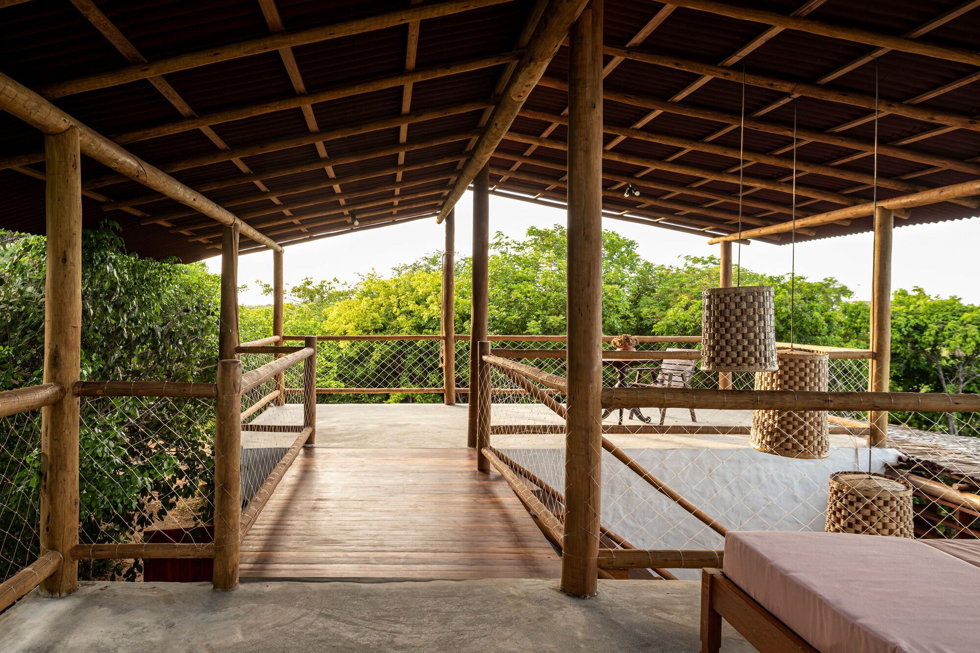 Upper-level terrace with timber columns, mesh railings, suspended woven lights and hammocks overlooking vegetation