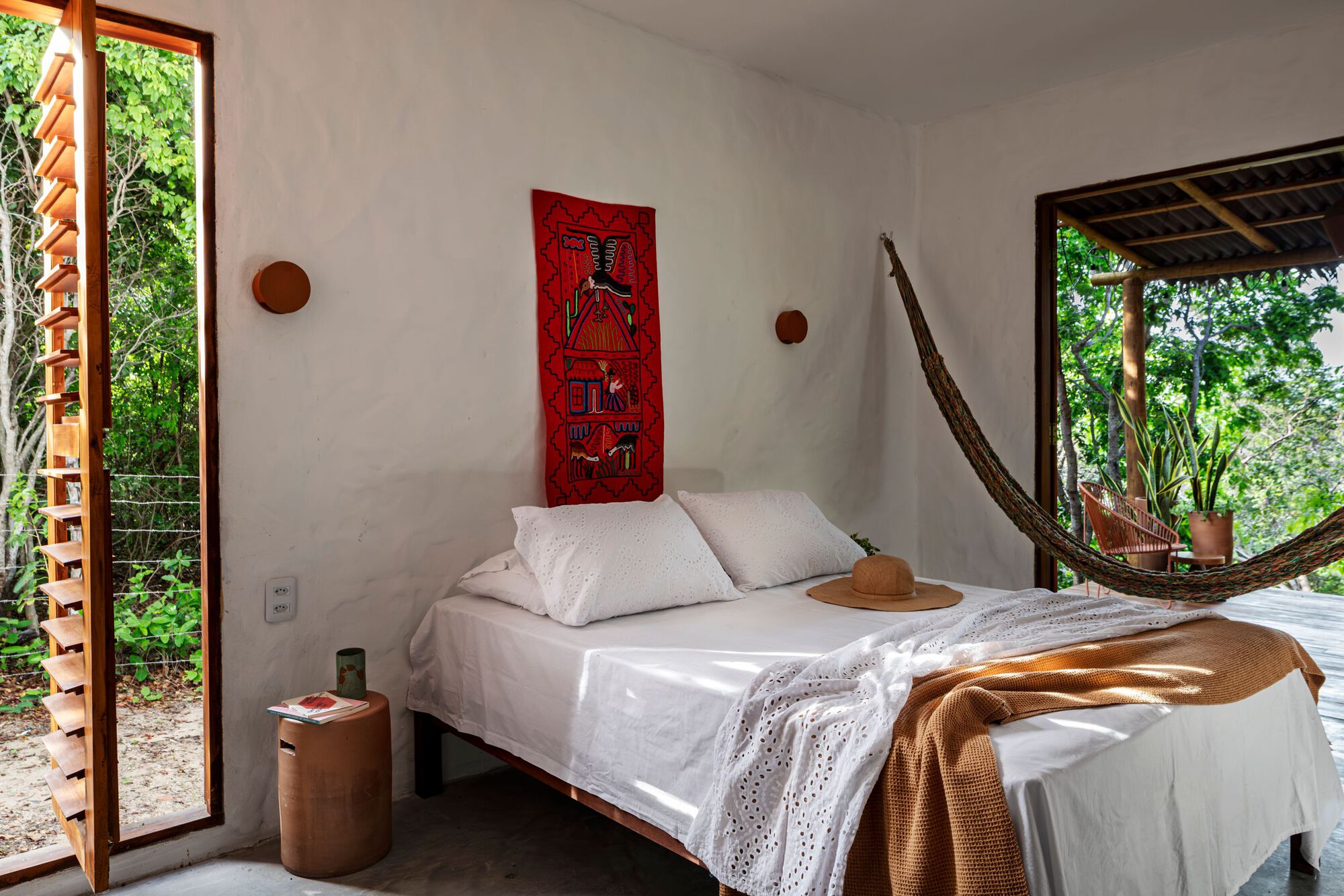 Bedroom with hammock and lattice timber doors opening to surrounding greenery in afternoon light