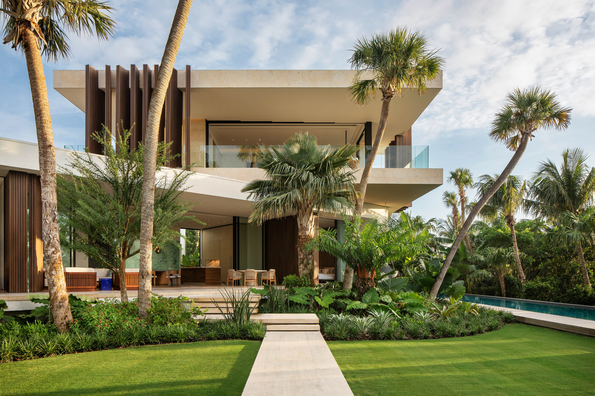 Garden view of the two-story residence with vertical timber screen and horizontal concrete balconies among palm trees