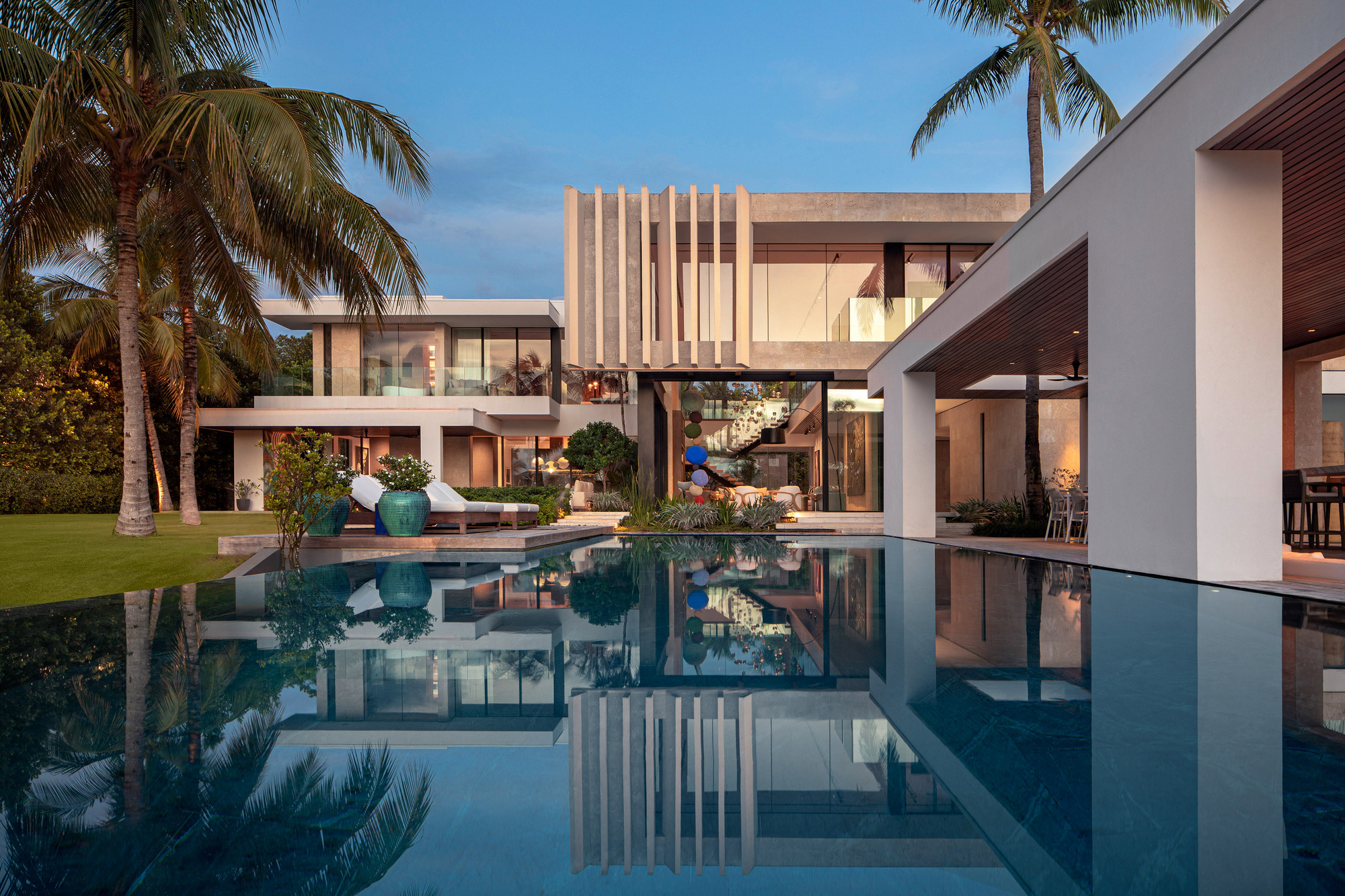 Rear courtyard view with reflecting pool and palm trees framing the multi-level residence at dusk