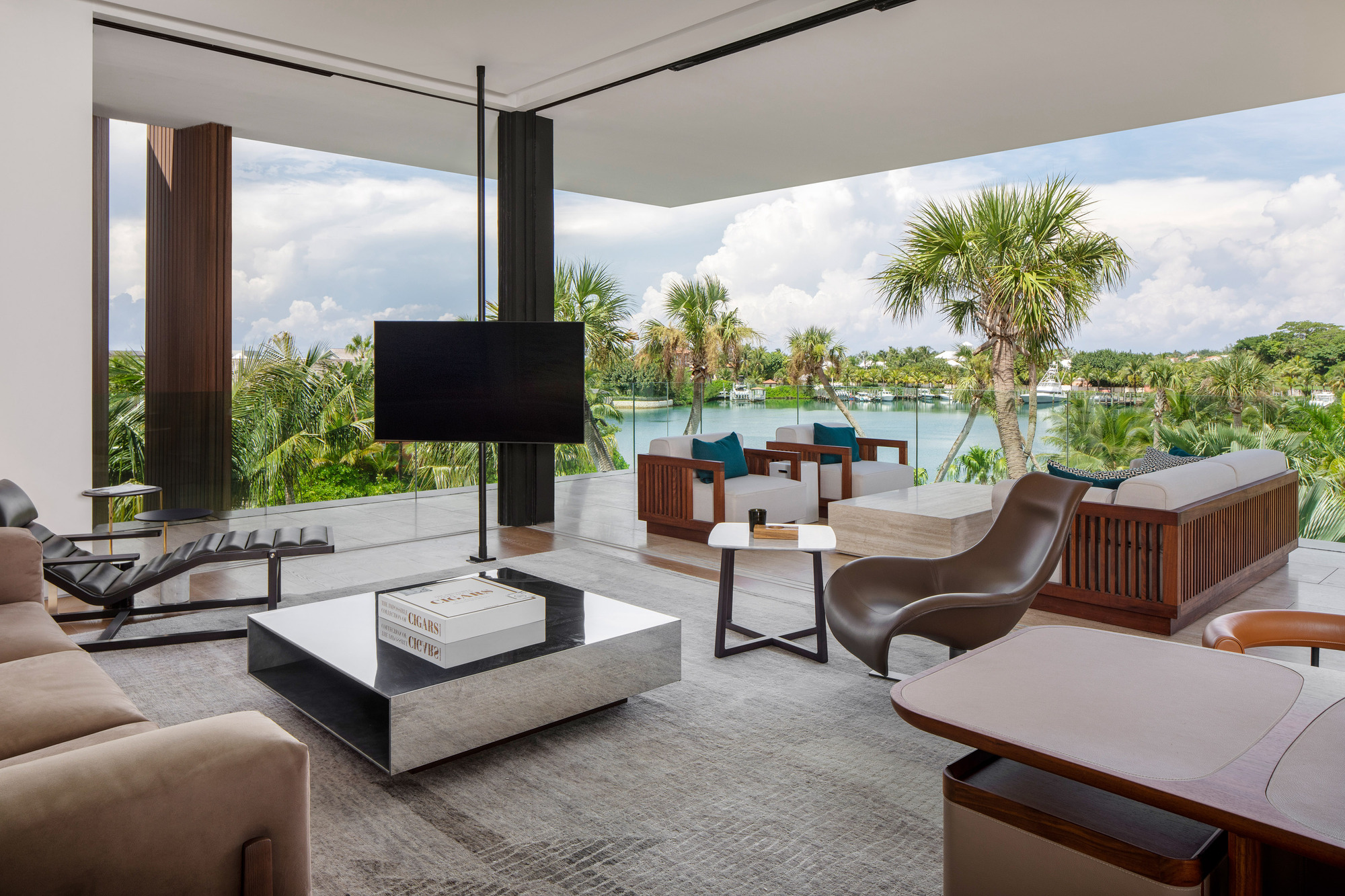 Open-plan living area with floor-to-ceiling glass walls overlooking lake and palm grove