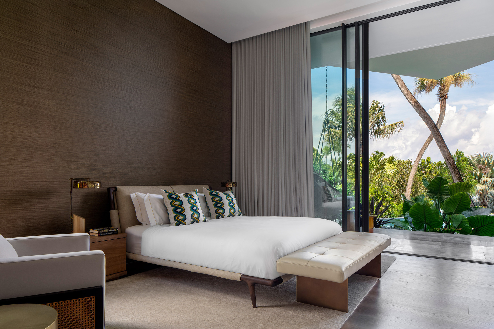 Bedroom with ribbed wood headboard wall and sliding glass doors to palm-shaded balcony