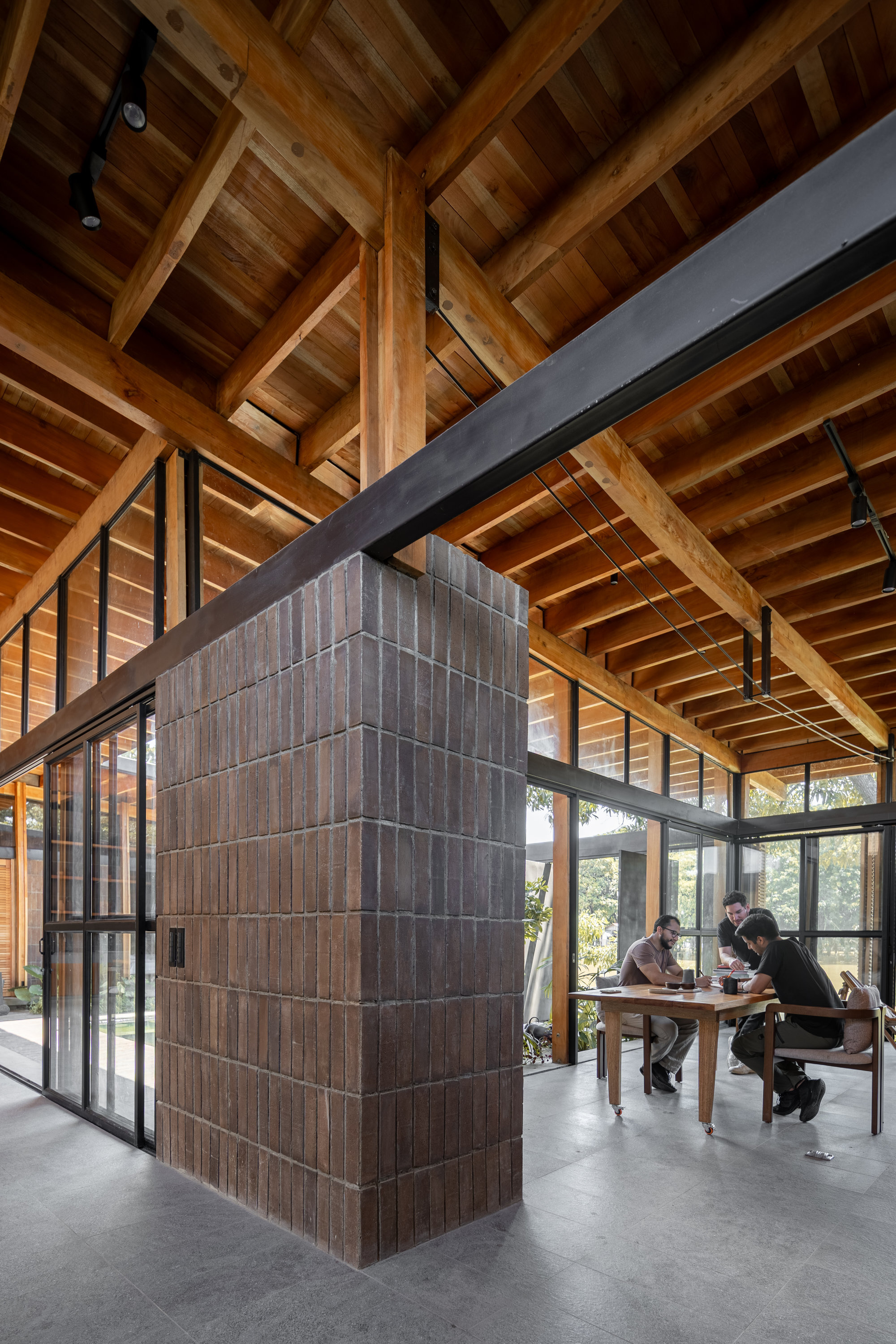 Vertical timber-clad core beneath crossing steel beams and a coffered wood ceiling with occupants nearby