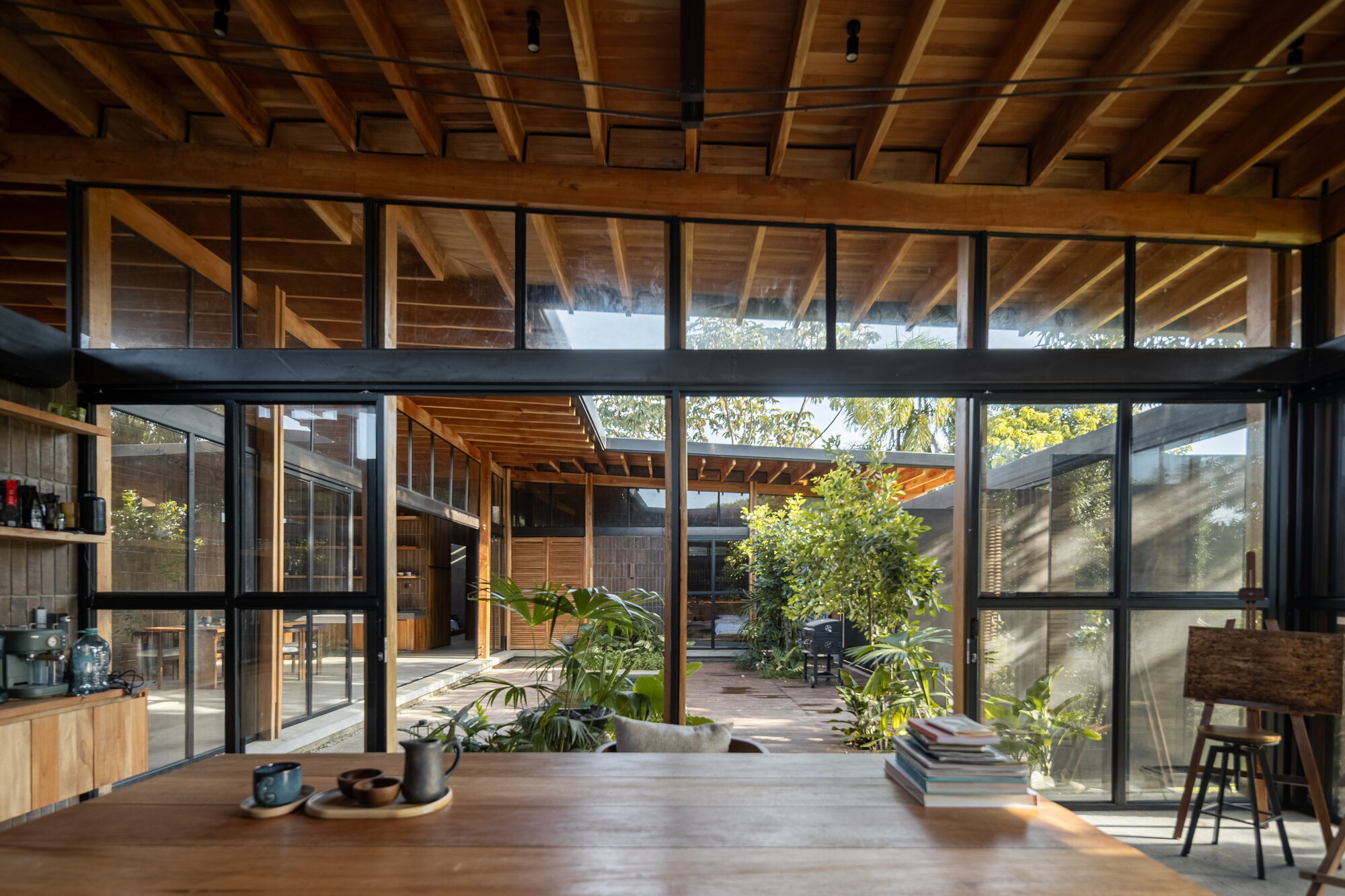 Interior living space with exposed timber ceiling and full-height glazing overlooking a planted courtyard
