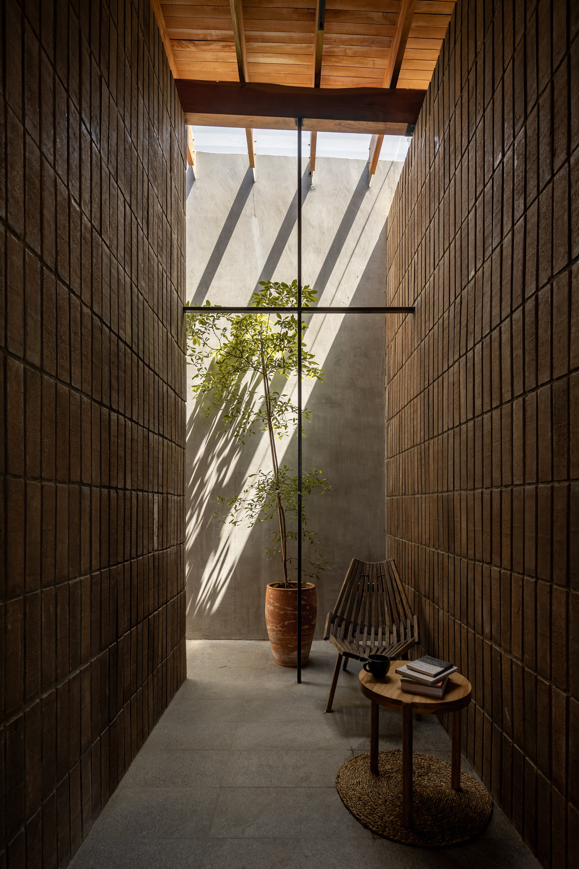 Narrow courtyard with vertical timber and brick walls, receiving angled shadows from overhead timber beams