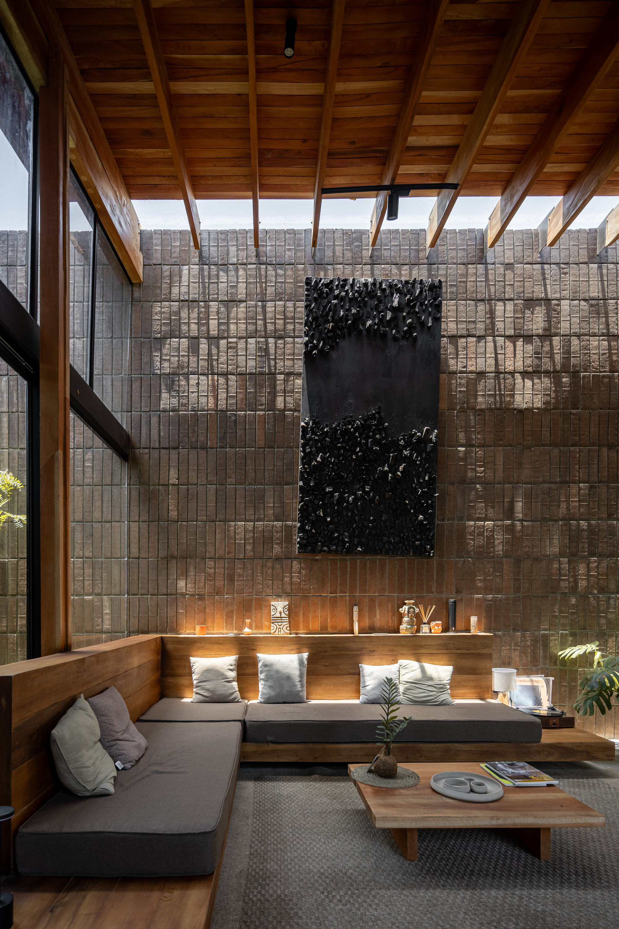 Double-height living room with exposed timber rafters and a decorative panel mounted on the brick wall