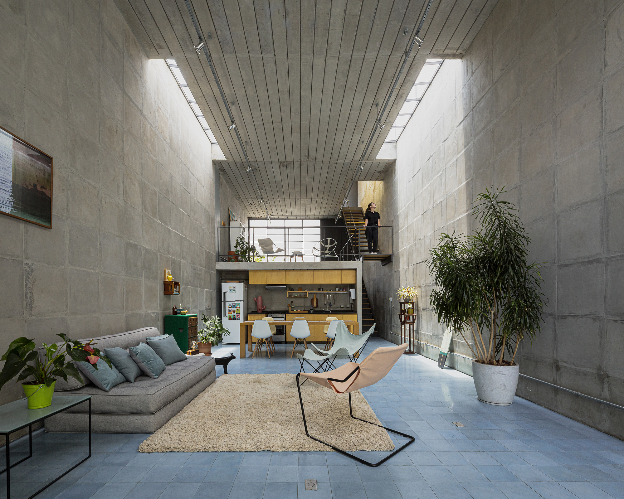 Double-height living space with concrete block walls, timber-slat ceiling and a steel mezzanine overlooking the dining area