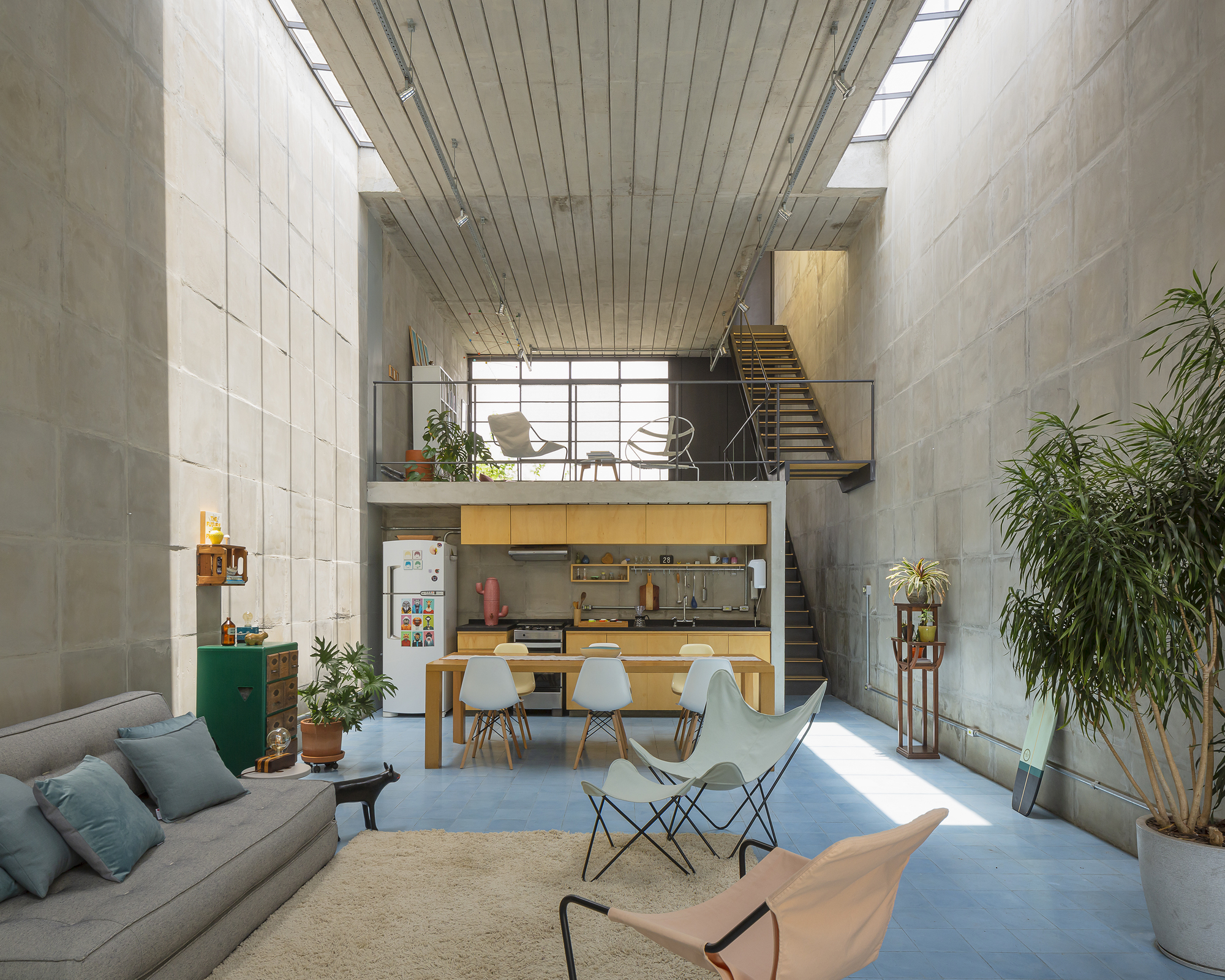 Open-plan interior showing mezzanine with timber stair and kitchen beneath slatted timber ceiling