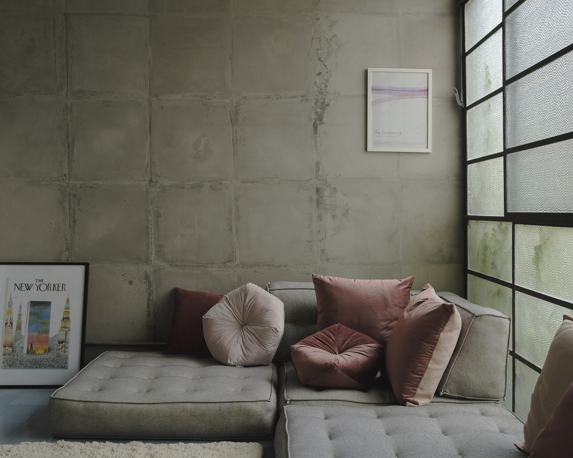 Corner seating area with board-formed concrete wall and translucent glass block window above grey sectional sofa