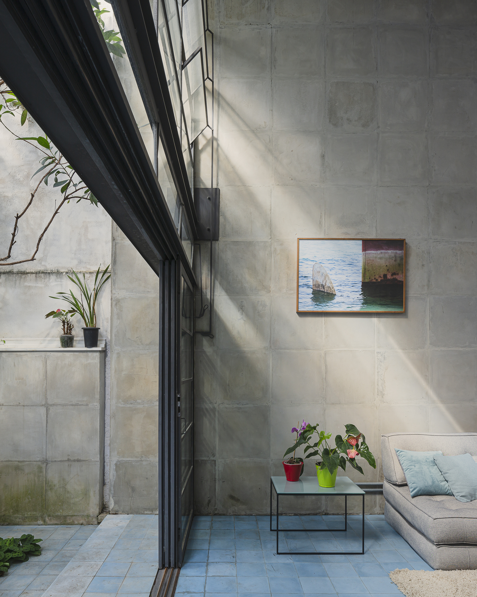 Double-height space with concrete block walls, black steel-framed glazing, and sunlight casting diagonal shadows