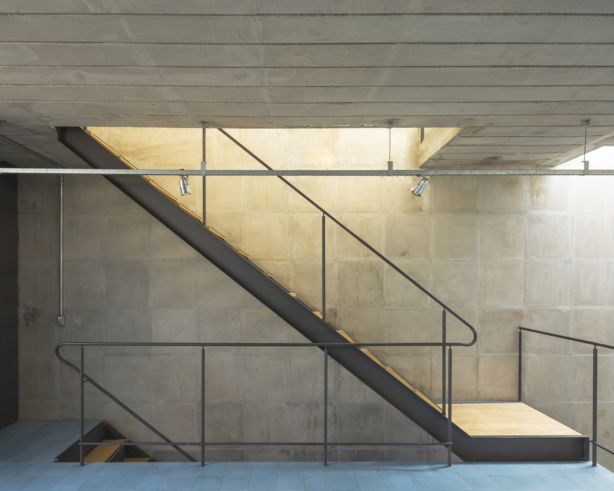 Steel staircase with tubular handrails and brass LED strip lighting against board-formed concrete walls