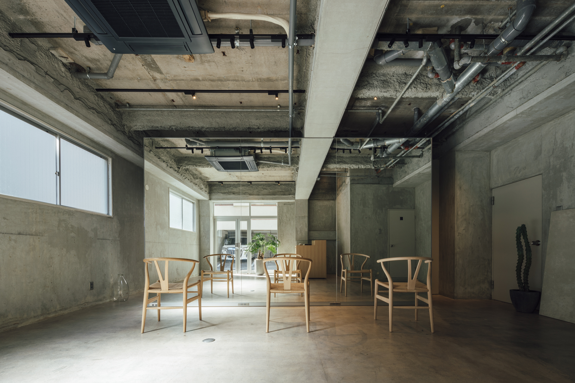 Interior with exposed concrete ceiling and mechanical systems above wooden chairs on polished floor