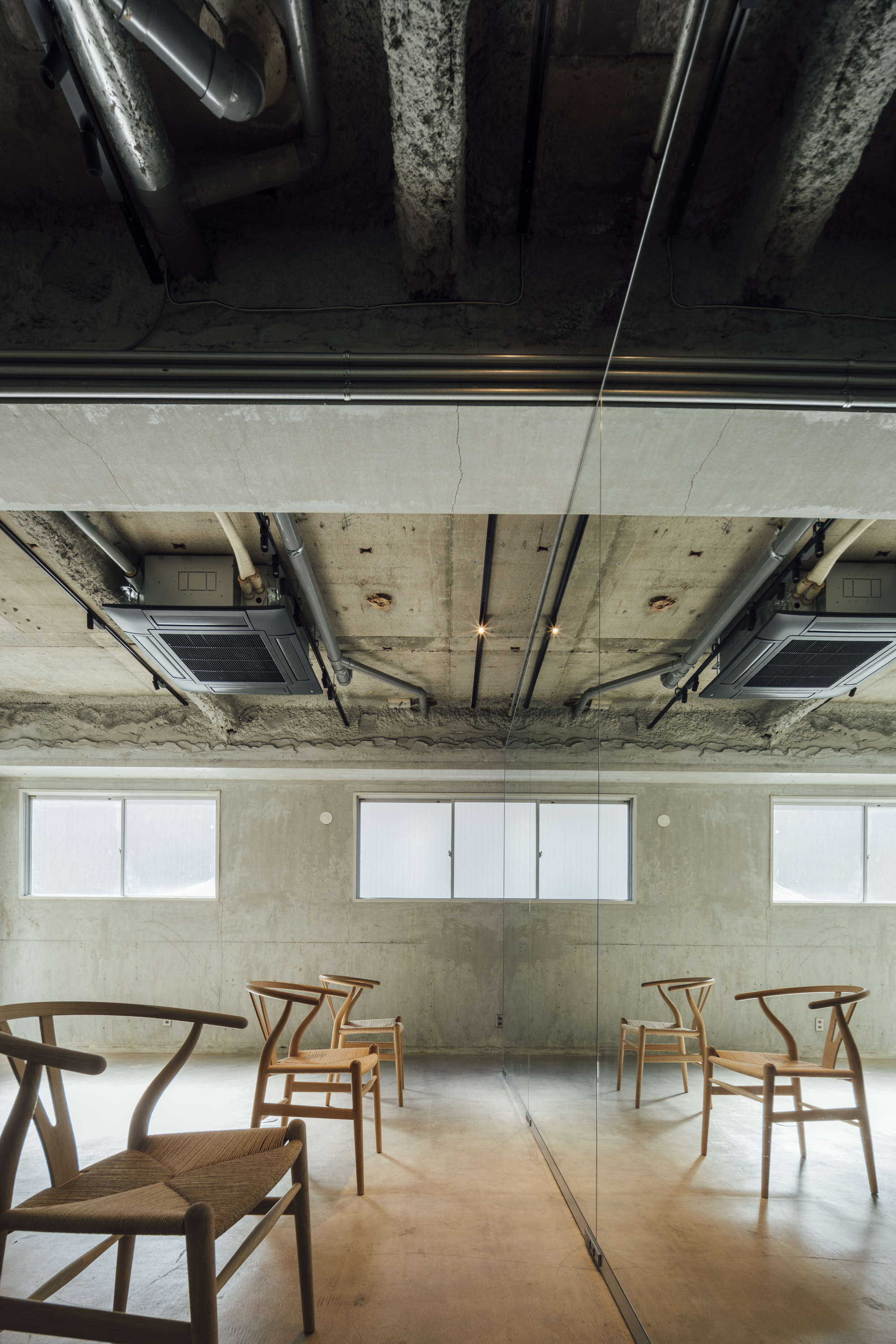 Overhead view showing the suspended white panel bisecting the concrete ceiling above arranged chairs