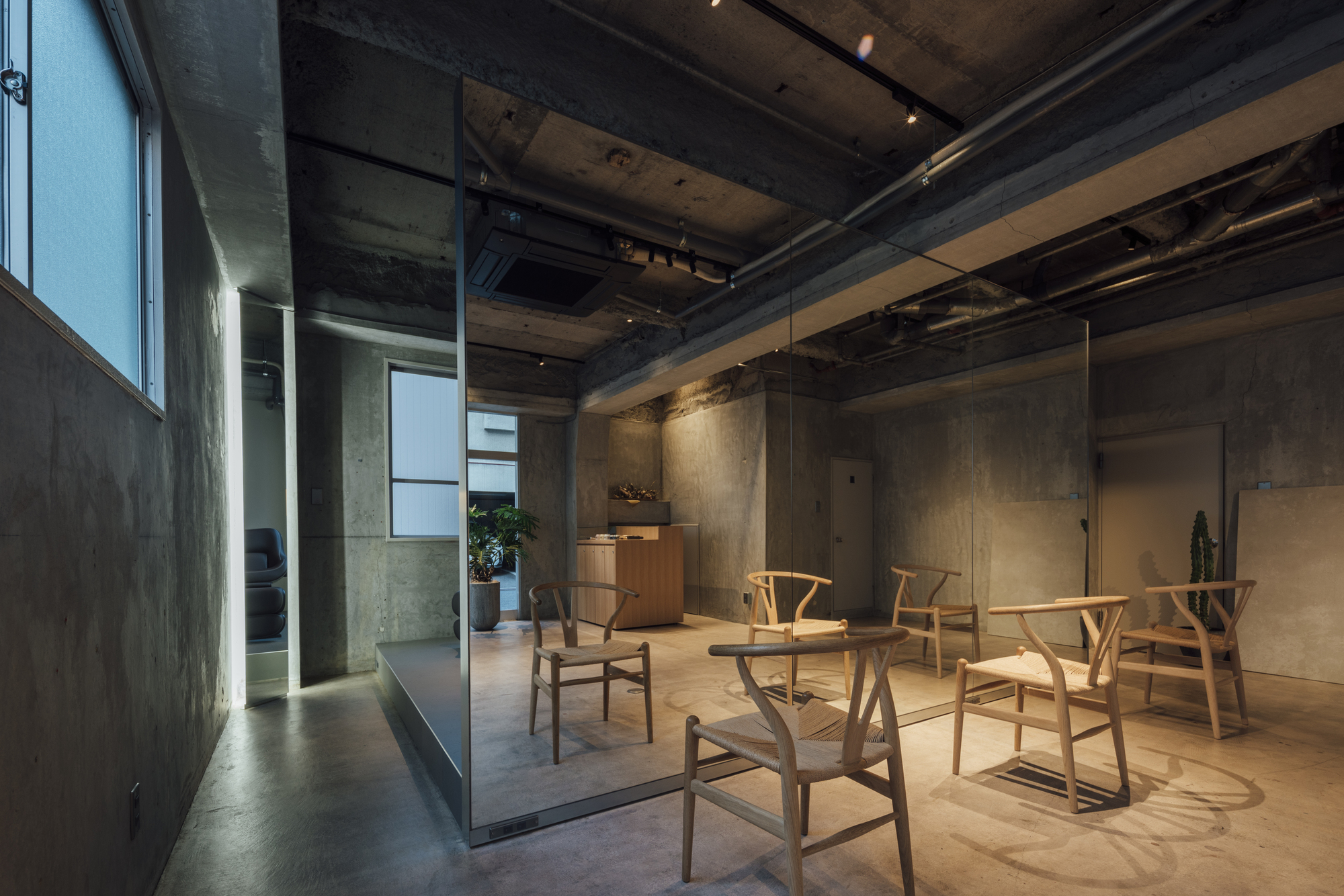 Interior at dusk with track lighting illuminating concrete walls and wooden furniture grouping