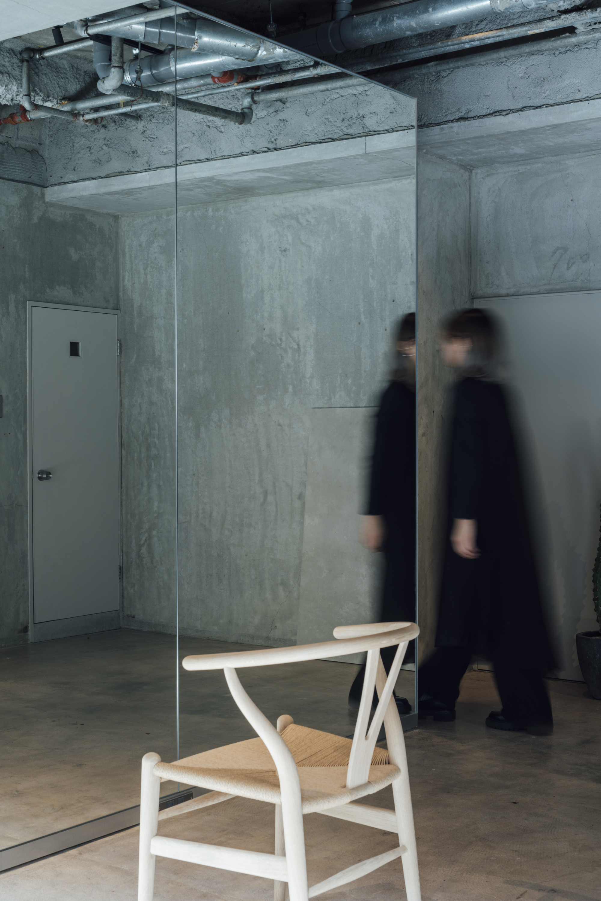 Single wooden chair behind glass panel with two figures in motion blur passing by