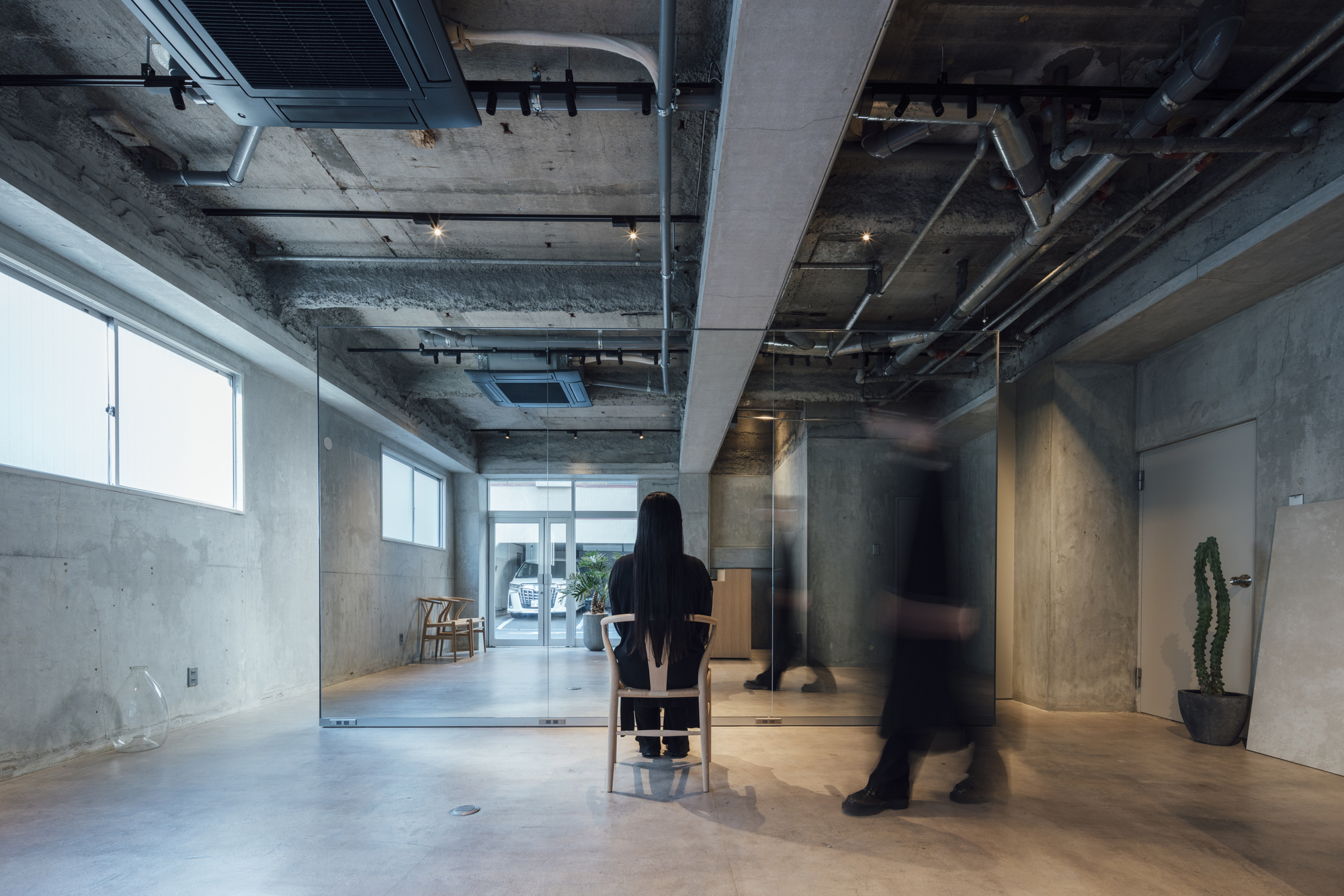 Long view through glass partitions with figure seated and another walking past in blur
