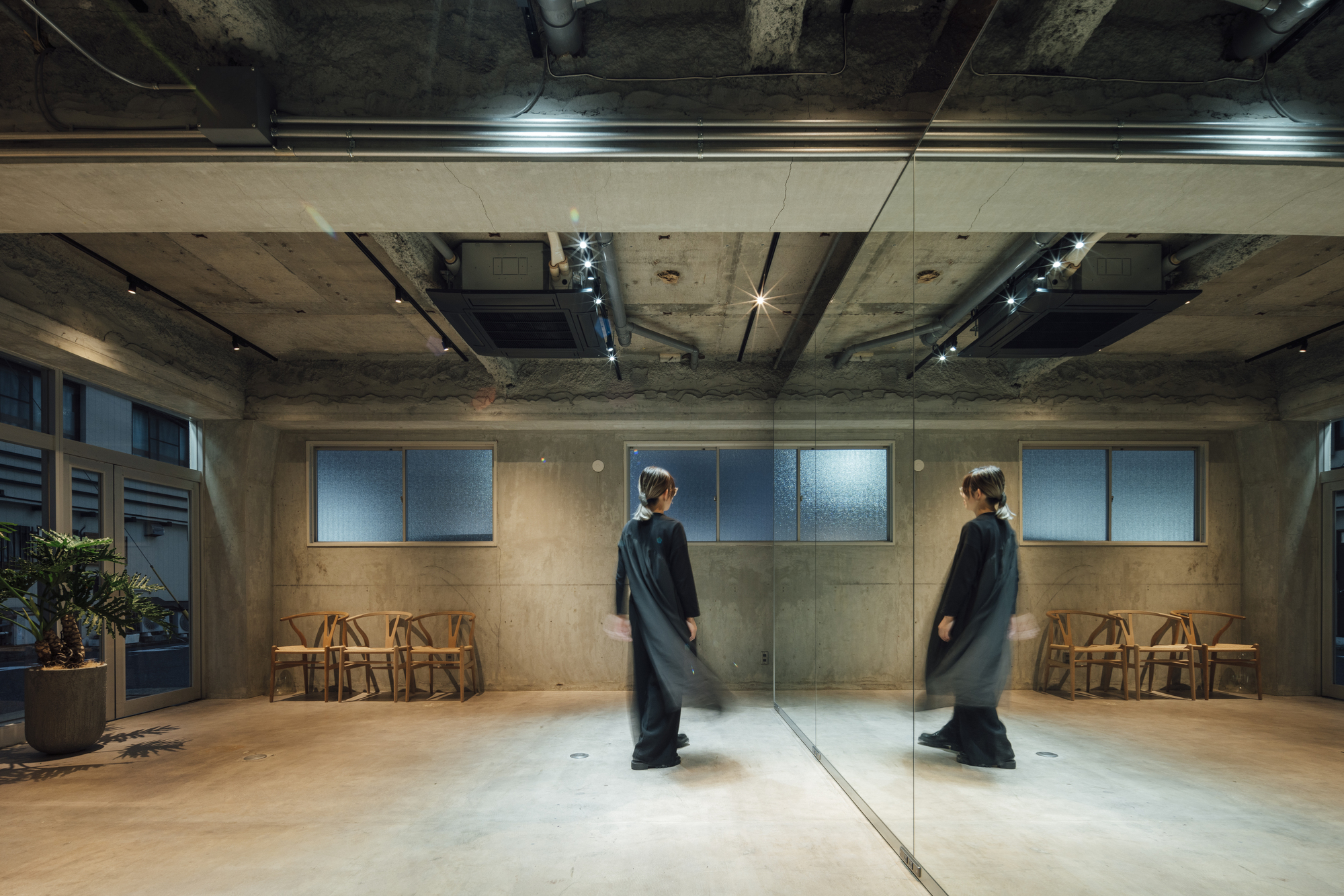 Interior space with exposed concrete ceiling and full-height mirror reflecting a figure in black
