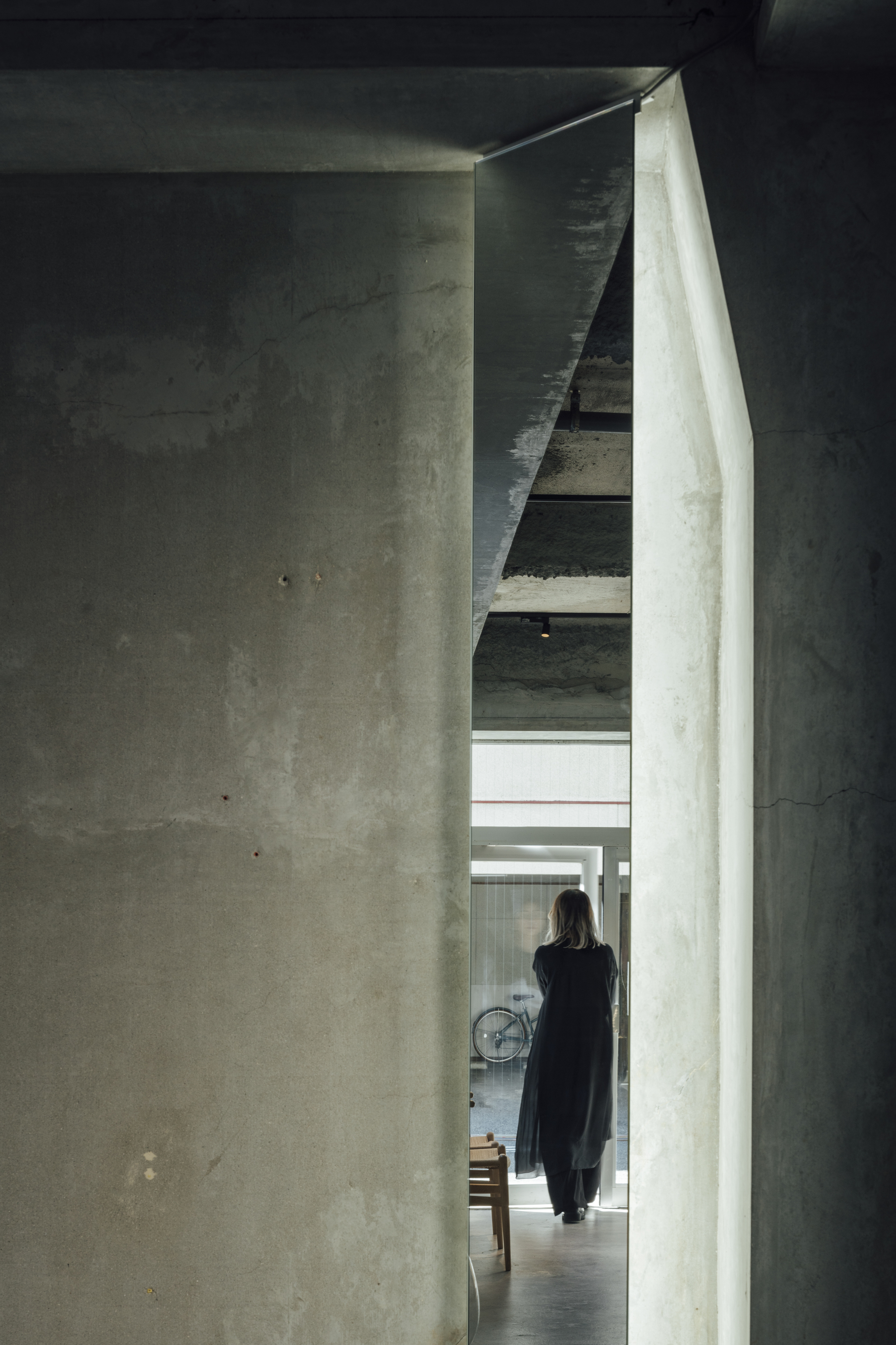 Narrow concrete passageway with a figure walking toward a staircase under indirect natural light