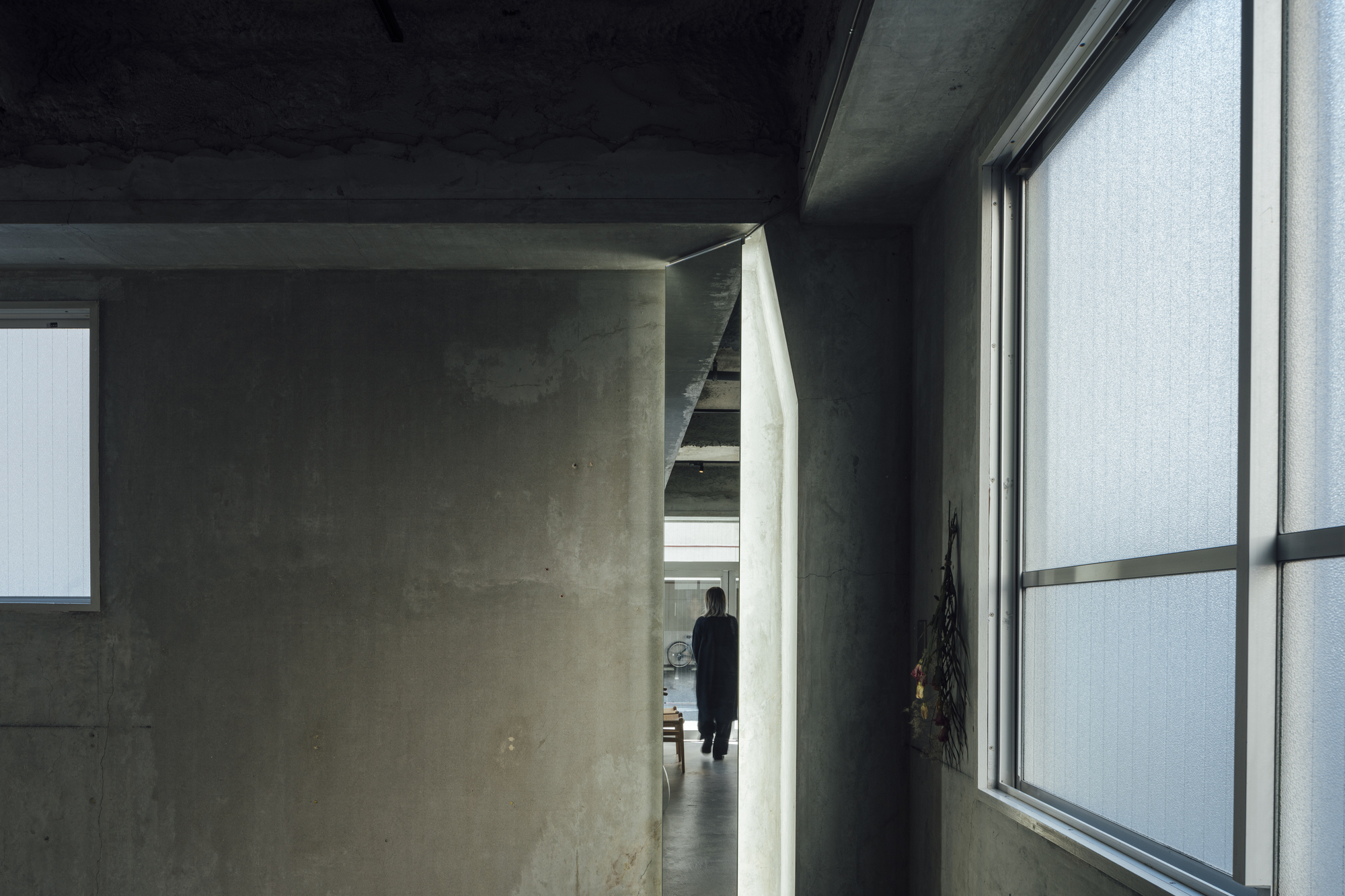 Concrete corridor with a figure visible through an angled doorway beneath a dark painted ceiling