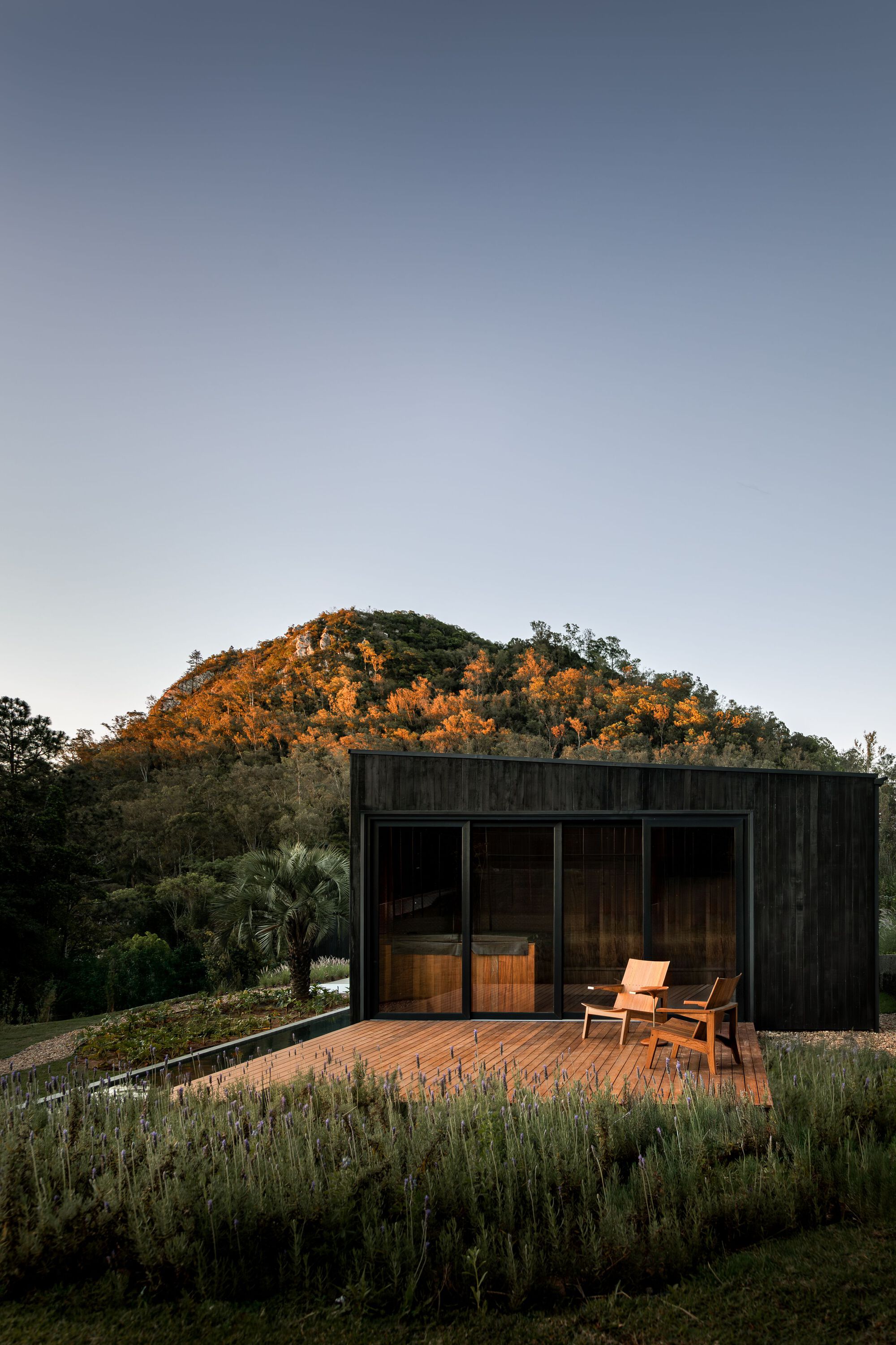 Timber deck with glazed openings and single chair facing illuminated hillside at dusk