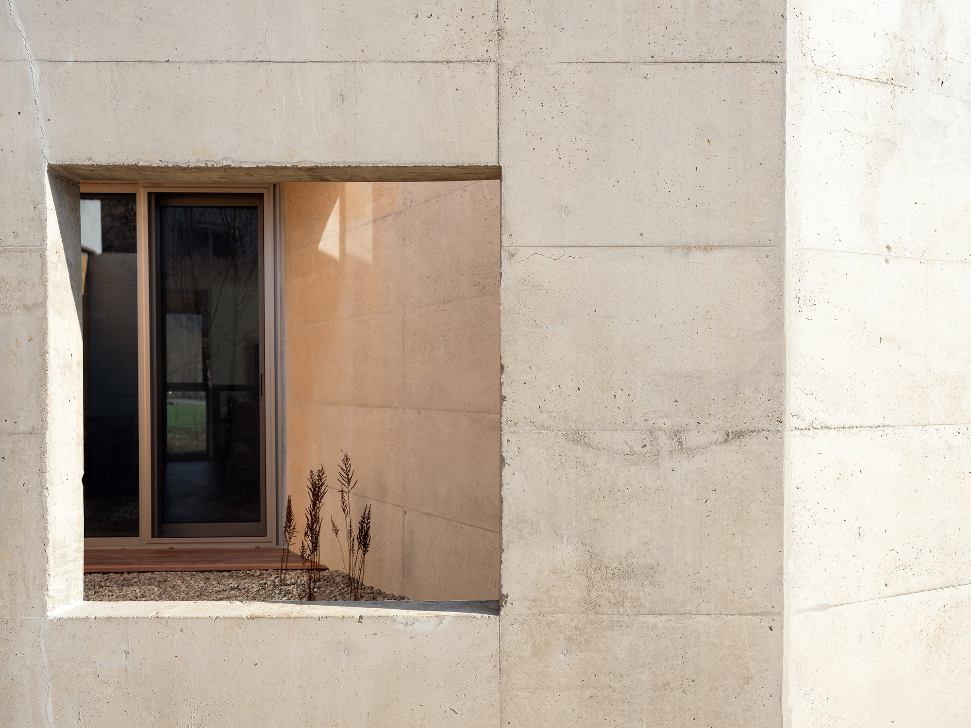 Recessed window opening in board-formed concrete wall with dried grasses in gravel sill