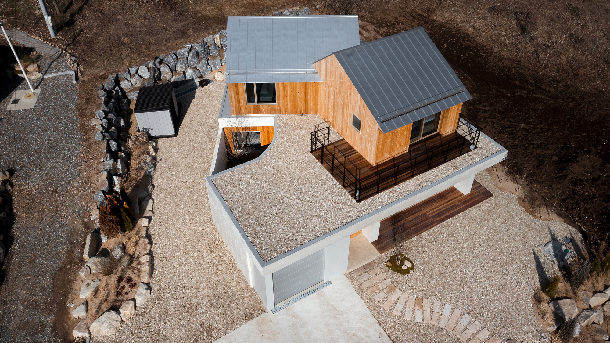 Aerial view of the residence showing gabled roofs, gravel terrace and stone retaining walls