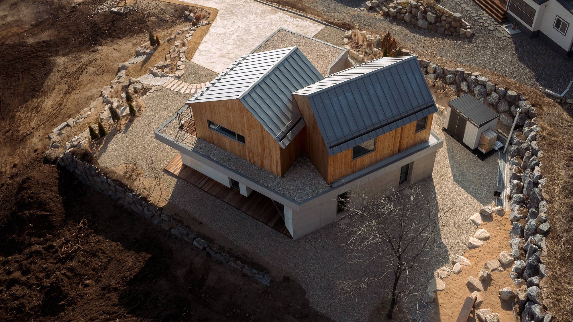 Drone view of the two gabled volumes with metal roofs sitting on a concrete plinth