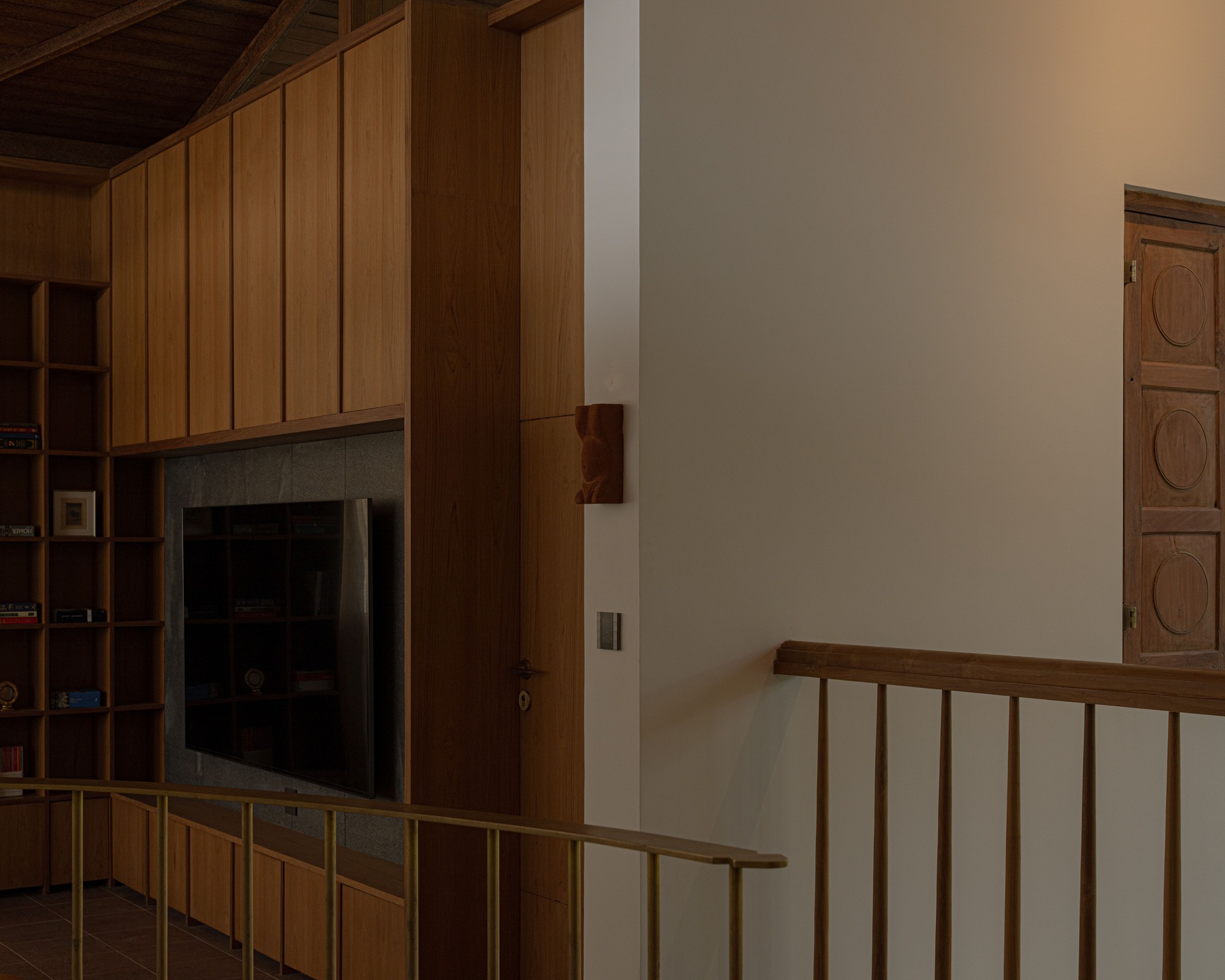 Timber staircase railing beside a built-in cabinetry wall with recessed television niche in dim light