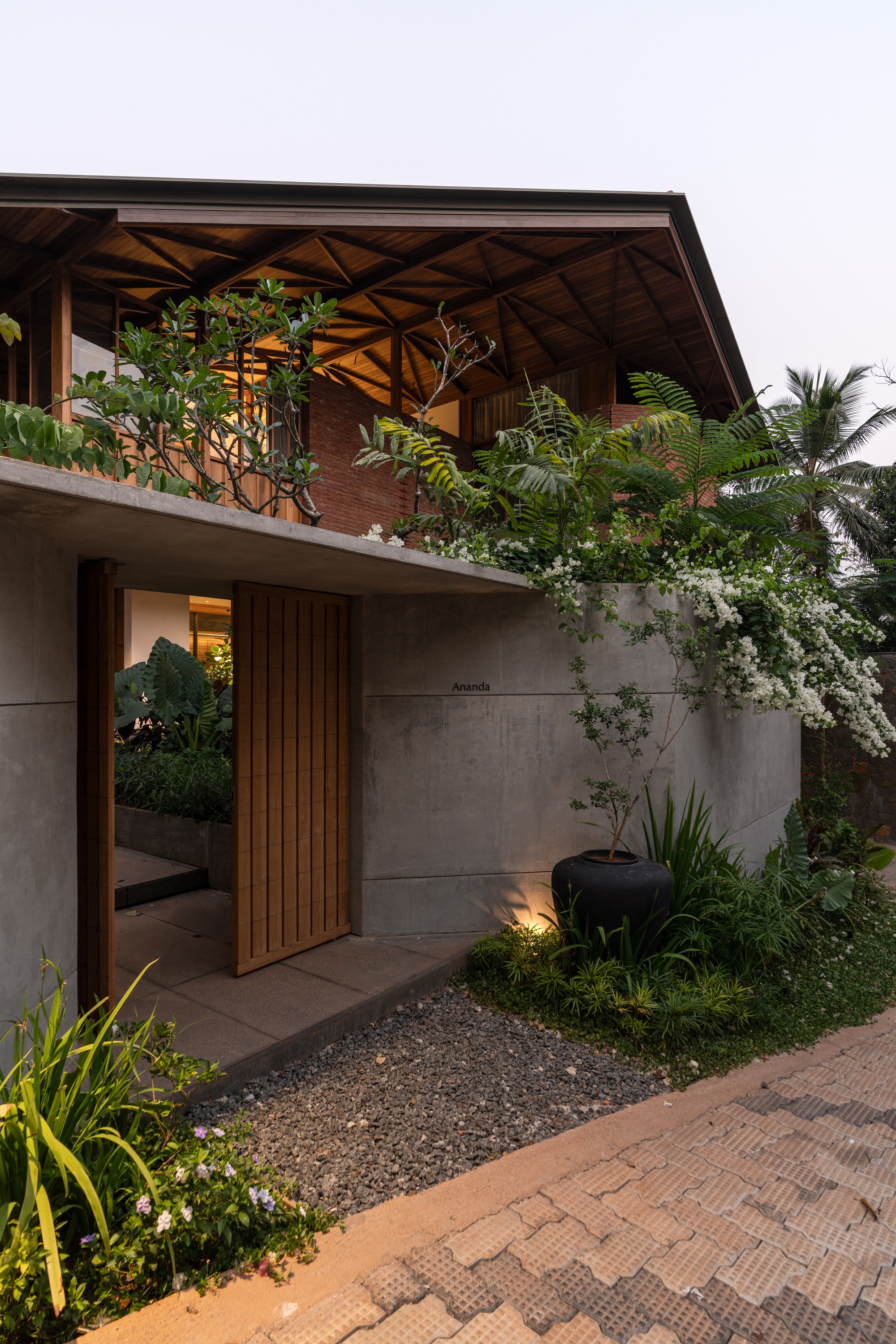 Concrete entrance wall with timber slat door and planted terrace balcony above at dusk