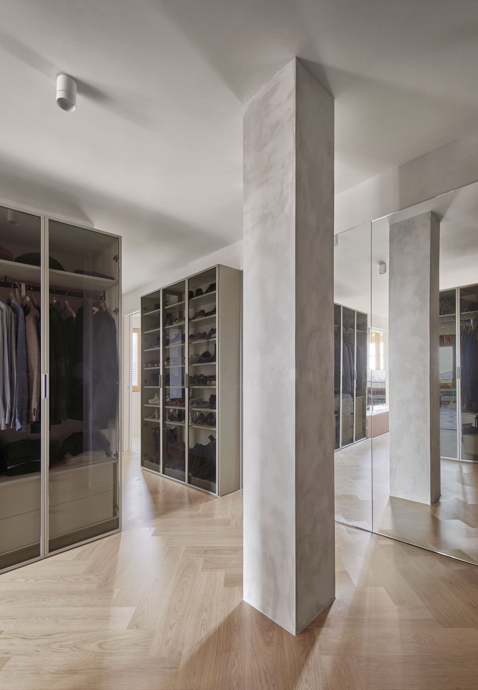 Dressing room with mirrored wardrobes and freestanding terrazzo-clad column on herringbone oak flooring