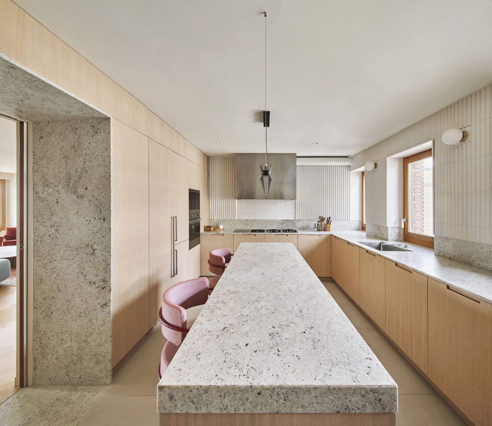 Galley kitchen with terrazzo island, oak cabinetry, fluted wall panels, and stainless steel range hood