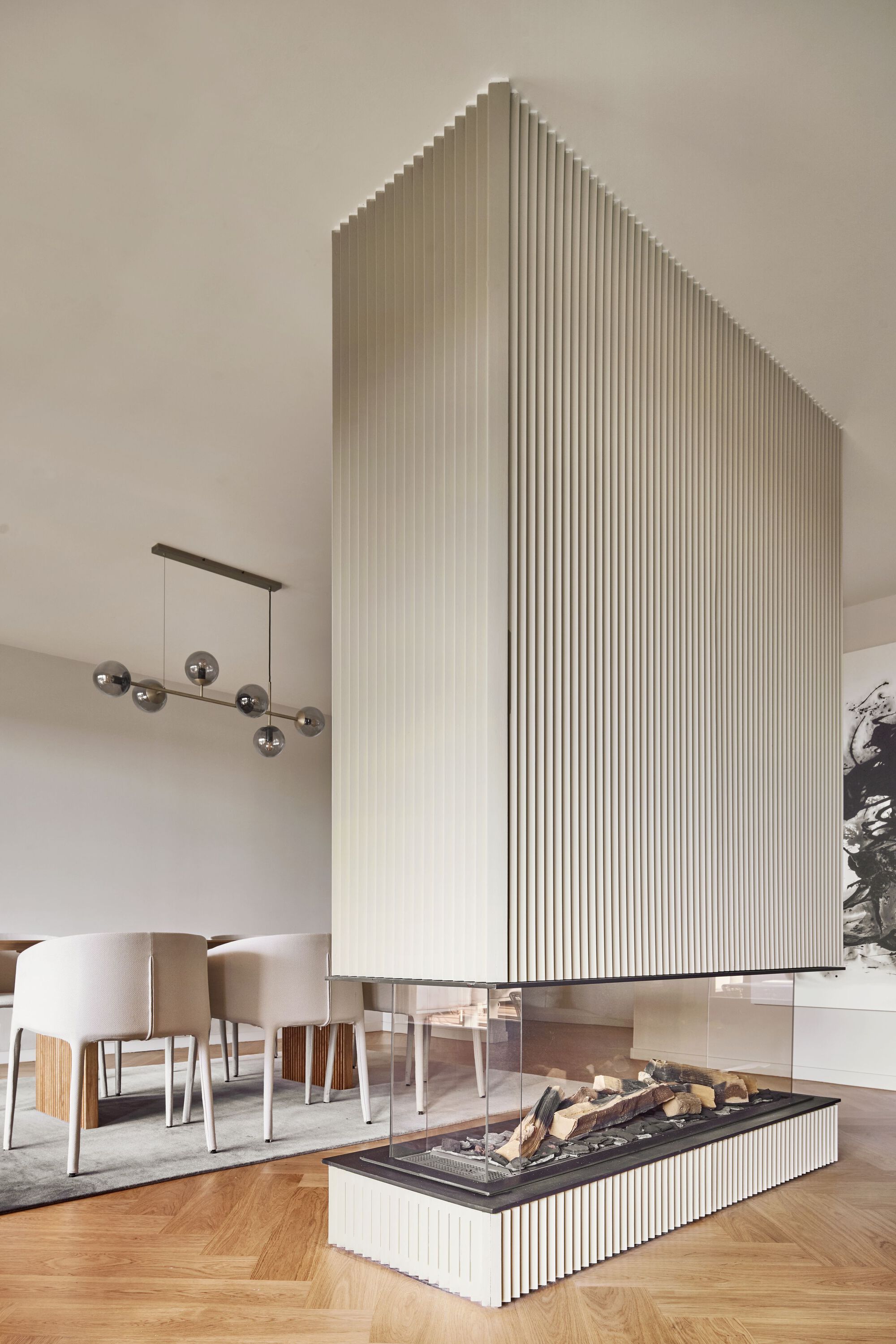 Fluted white fireplace column with black hearth and stacked firewood below a bronze pendant lamp