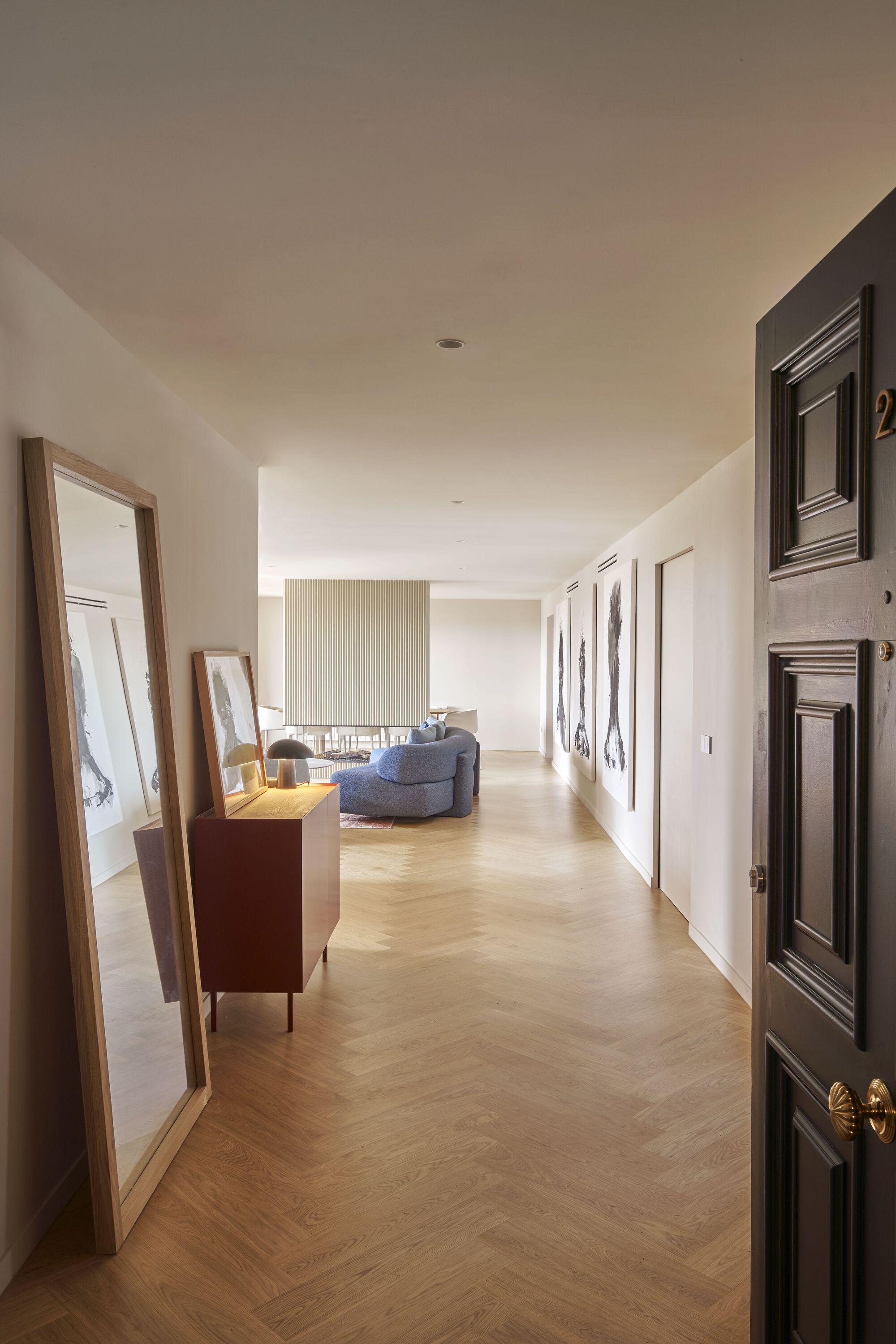 Long hallway with chevron parquet flooring and framed artwork leading to a seating area