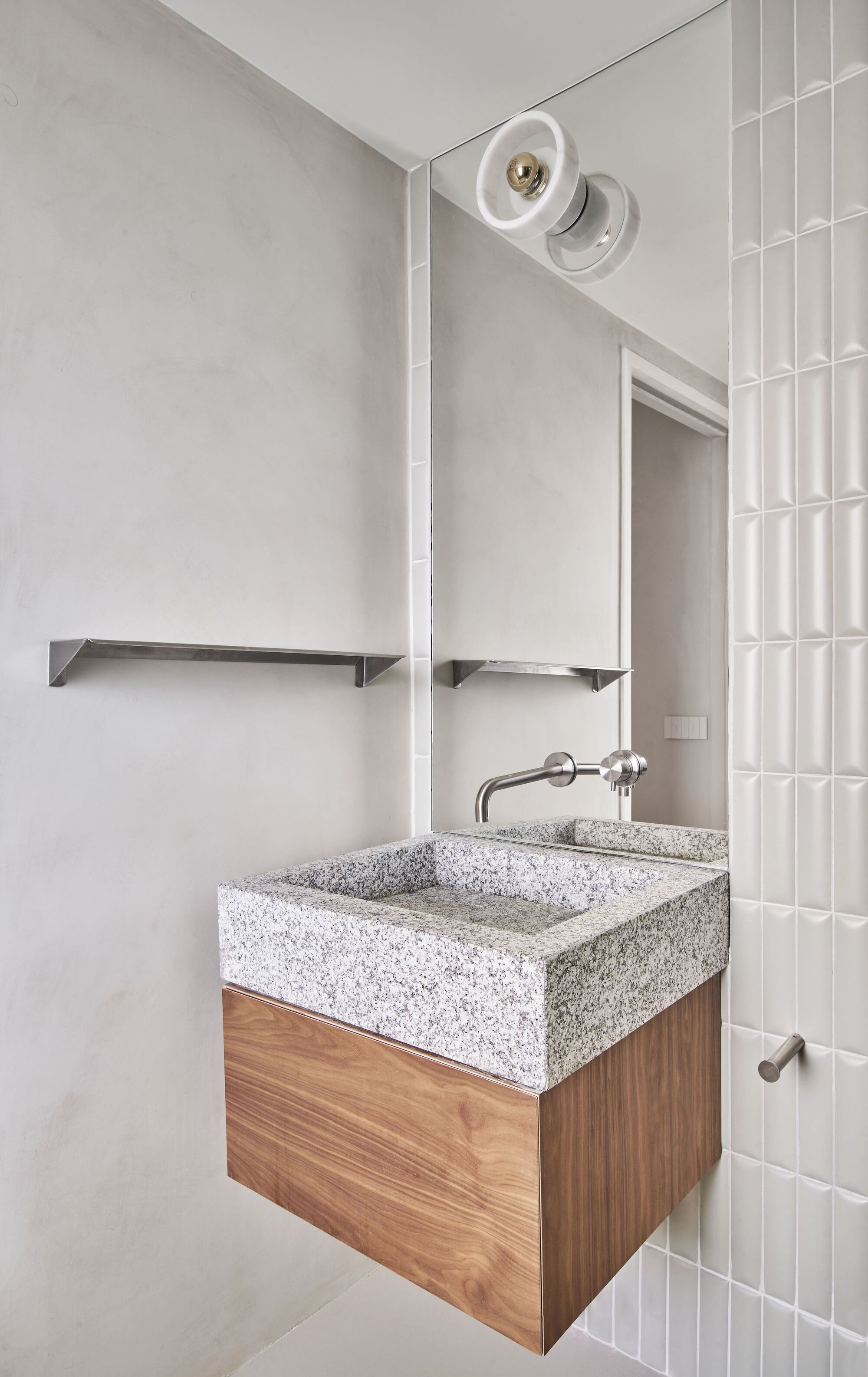 Bathroom vanity with terrazzo sink on timber cabinet beside vertical white tile wall