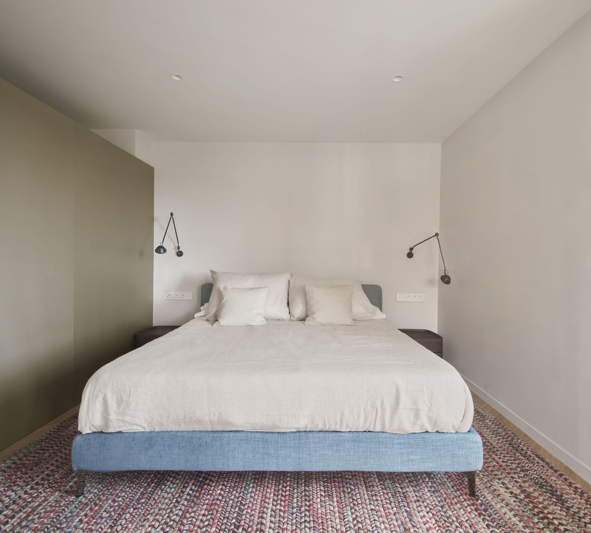 Bedroom with blue upholstered platform bed and articulated wall-mounted reading lamps
