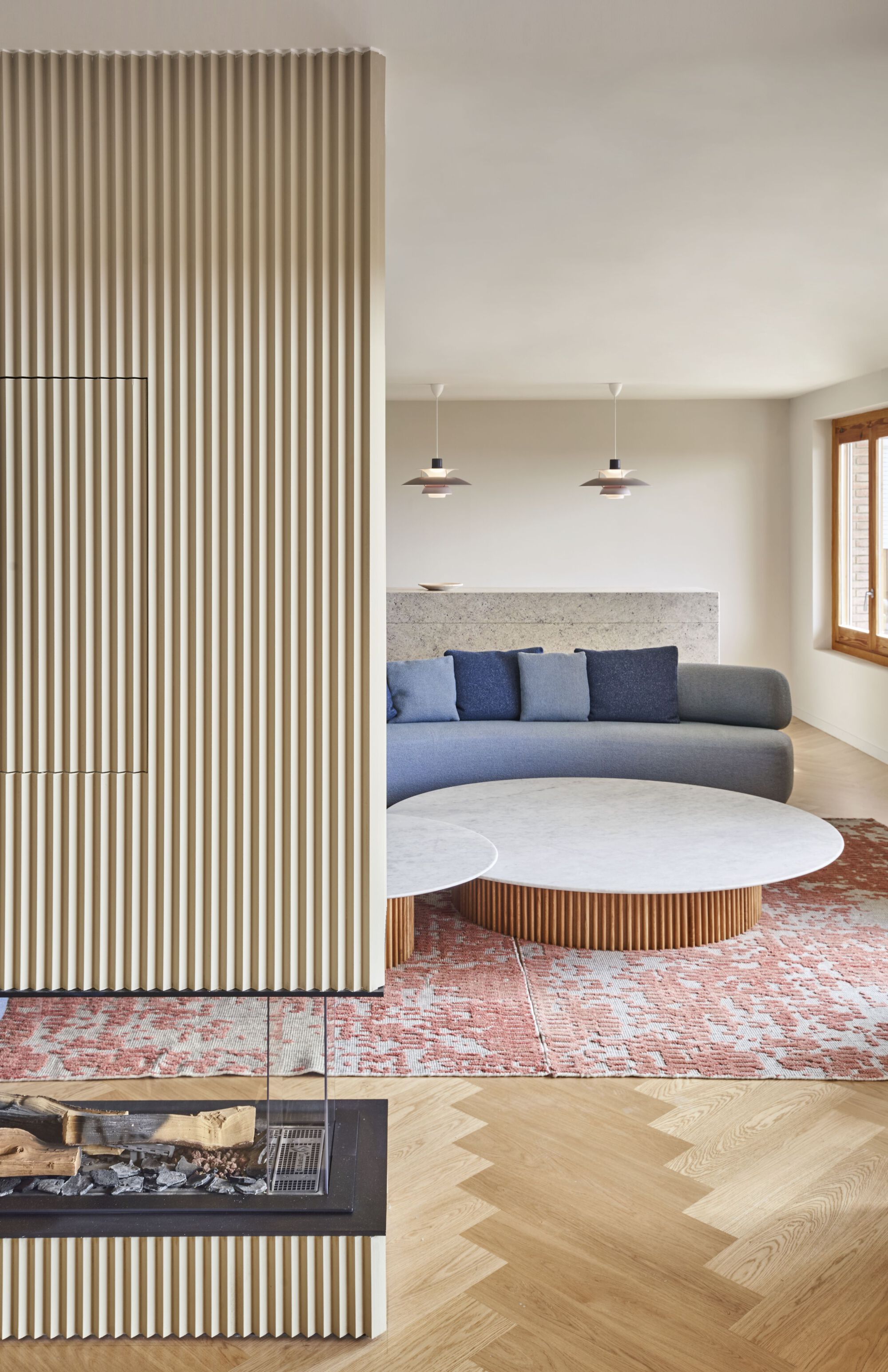 Living room with vertical fluted timber partition, curved sofa, and herringbone oak flooring over patterned rug