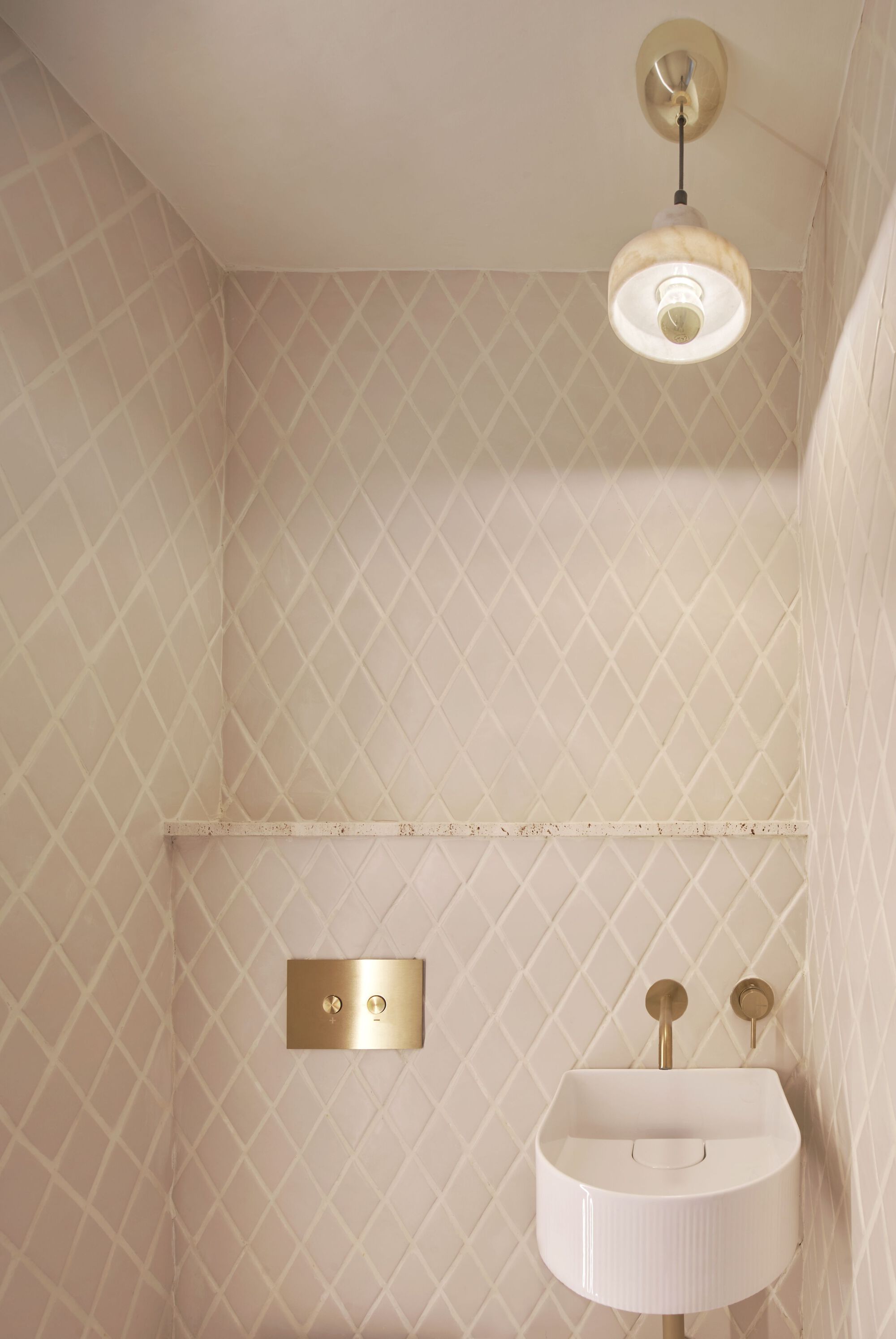 Compact bathroom with diamond-pattern tile walls, brass fixtures, and ribbed wall-mounted sink below pendant light