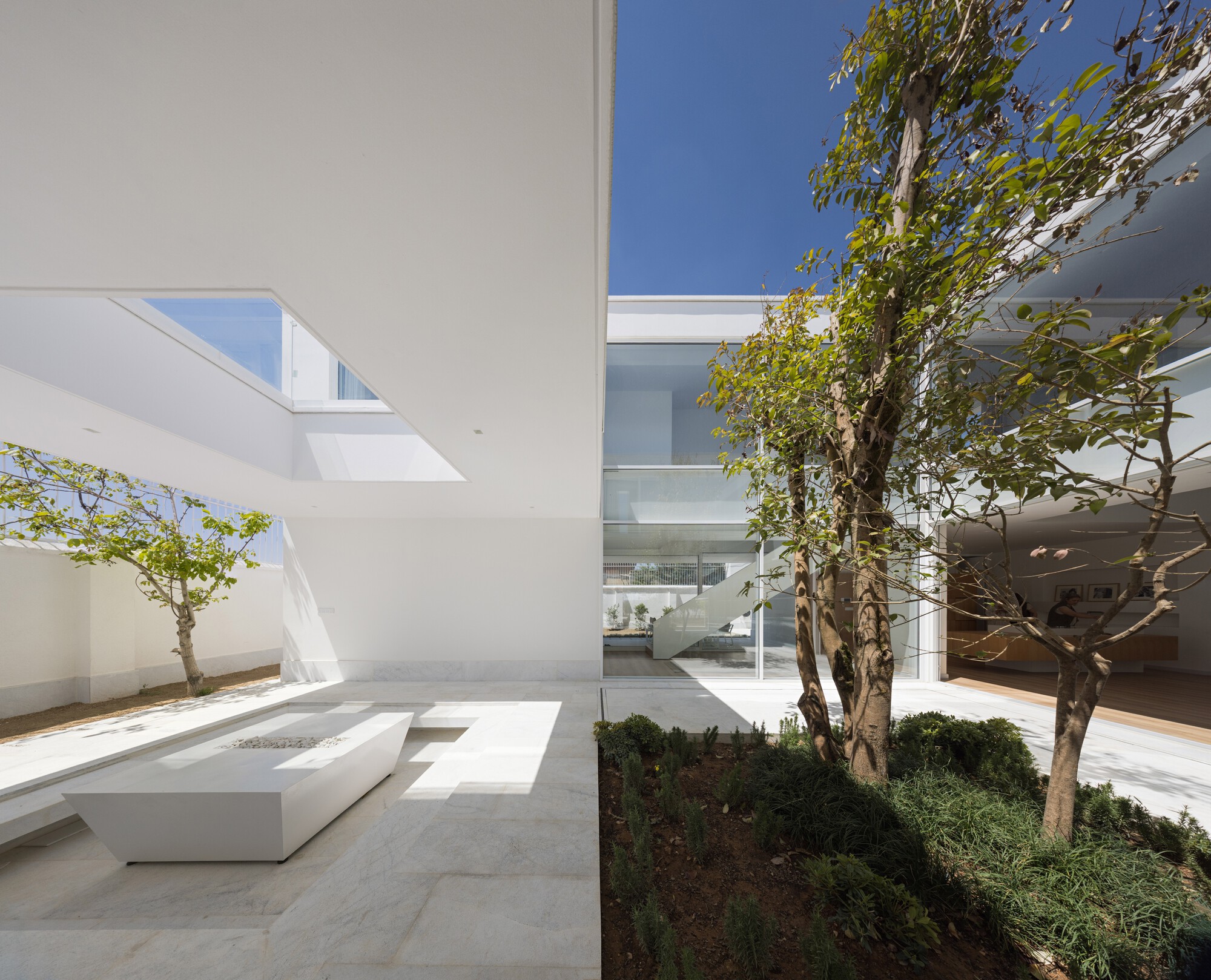 Interior courtyard with limestone paving and angular white planter facing trees and glazed volumes