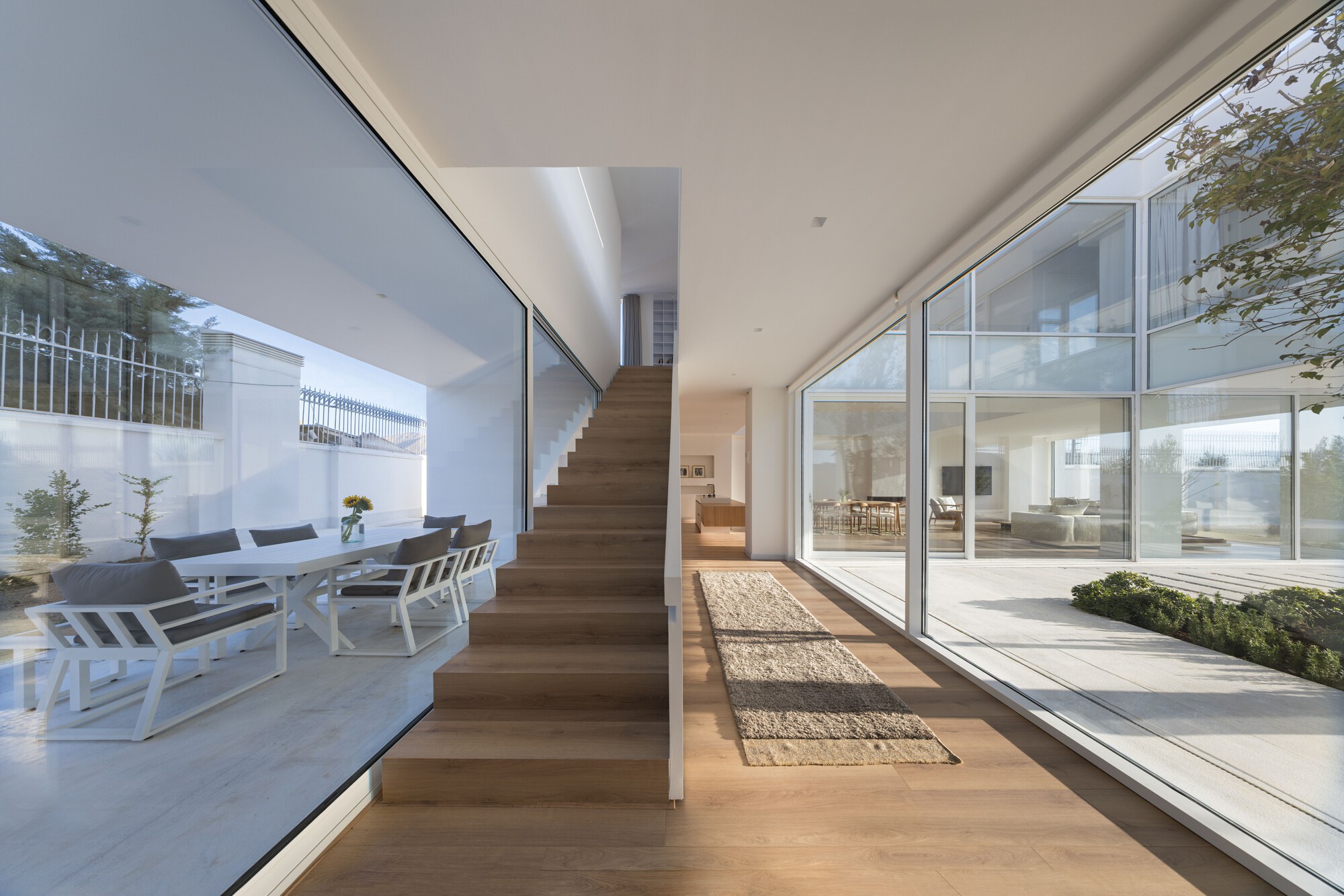 Timber staircase ascending beside floor-to-ceiling glazing overlooking a courtyard with outdoor seating