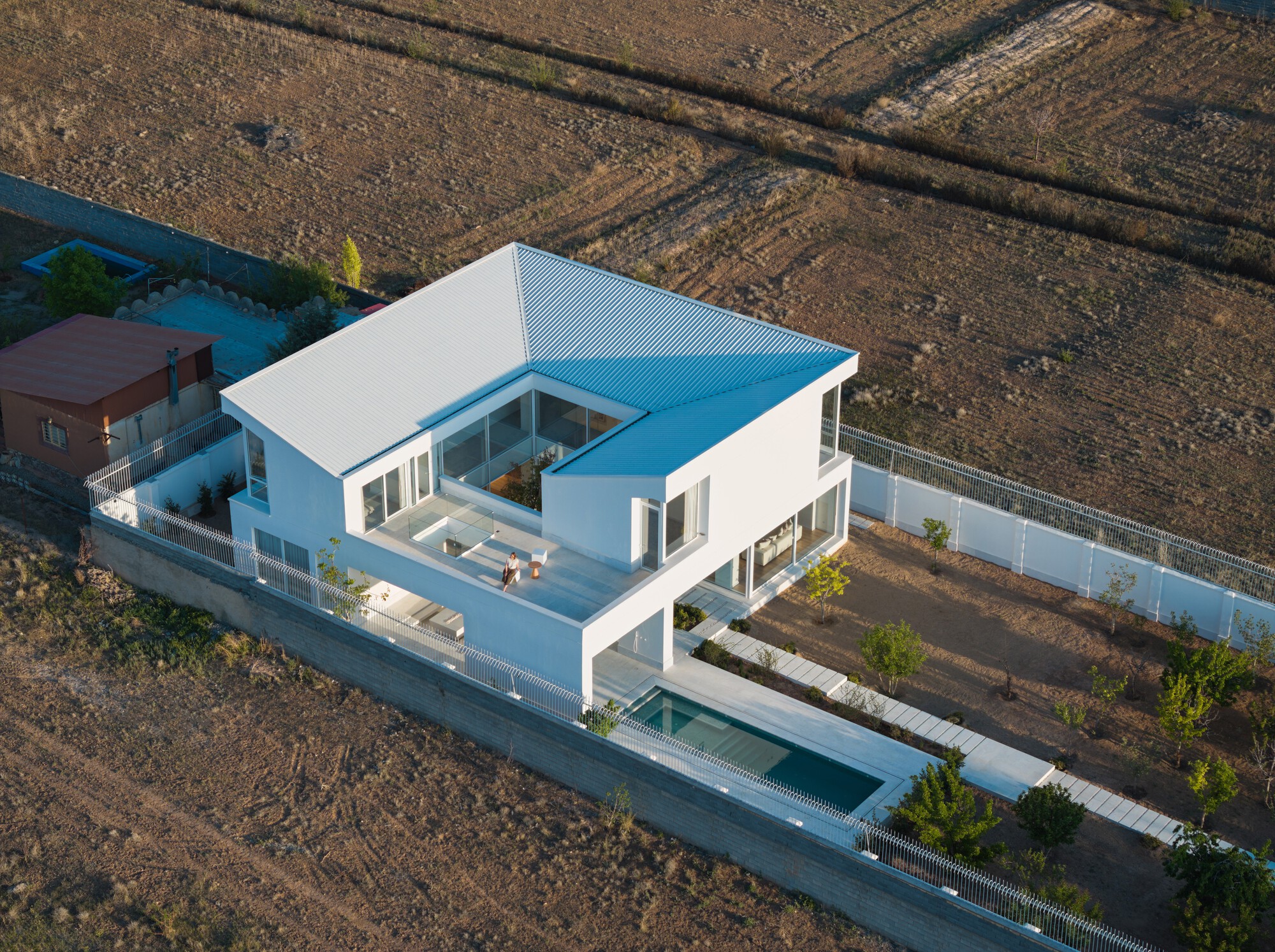 Aerial view of a two-story residence with a central courtyard surrounded by agricultural fields at dusk