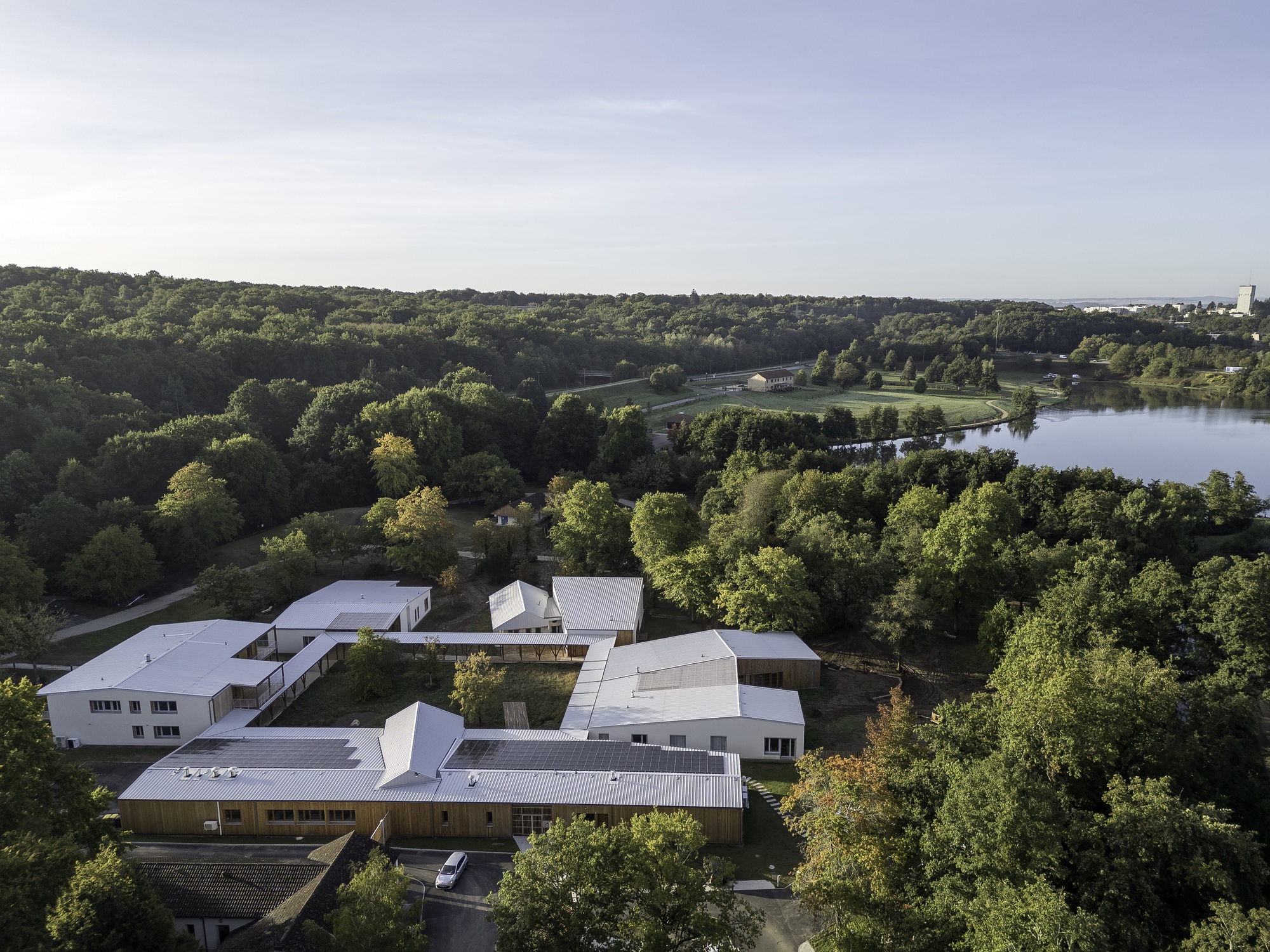 Aerial view of the interconnected white roof volumes nestled among dense forest and lake