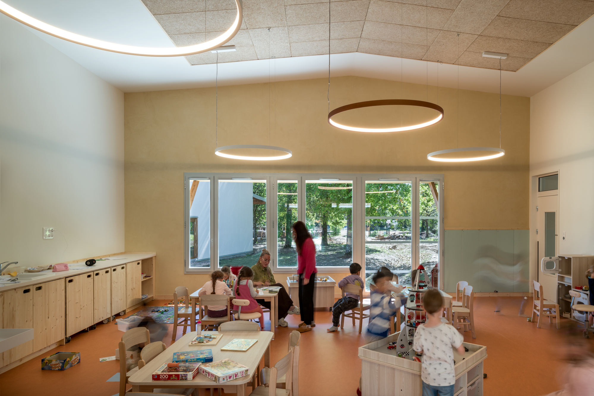 Classroom interior with circular pendant lights and children at play tables beneath a cork ceiling