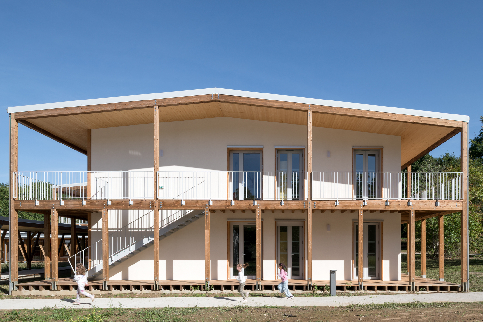 Two-storey timber structure with exposed wooden columns and elevated walkway under a clear blue sky