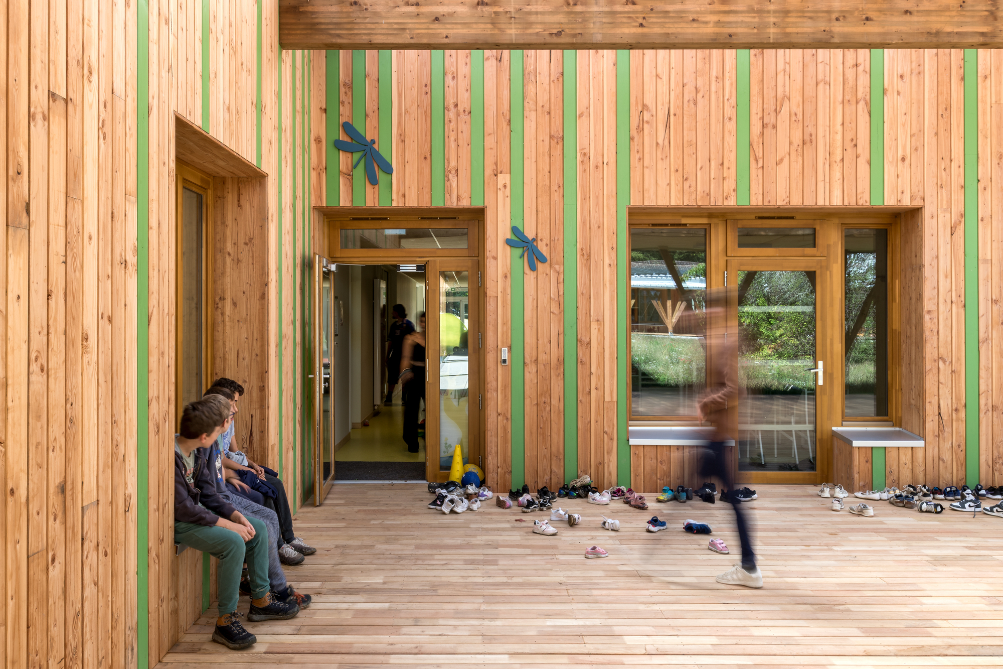 Wooden facade with green vertical stripes and scattered shoes on the deck as a child runs