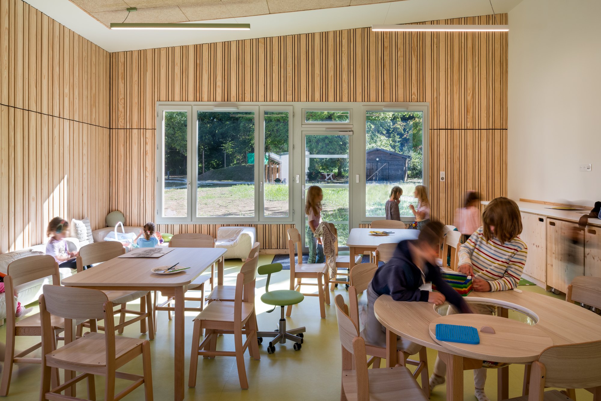 Classroom with striped timber wall panels and children seated at wooden tables on green flooring